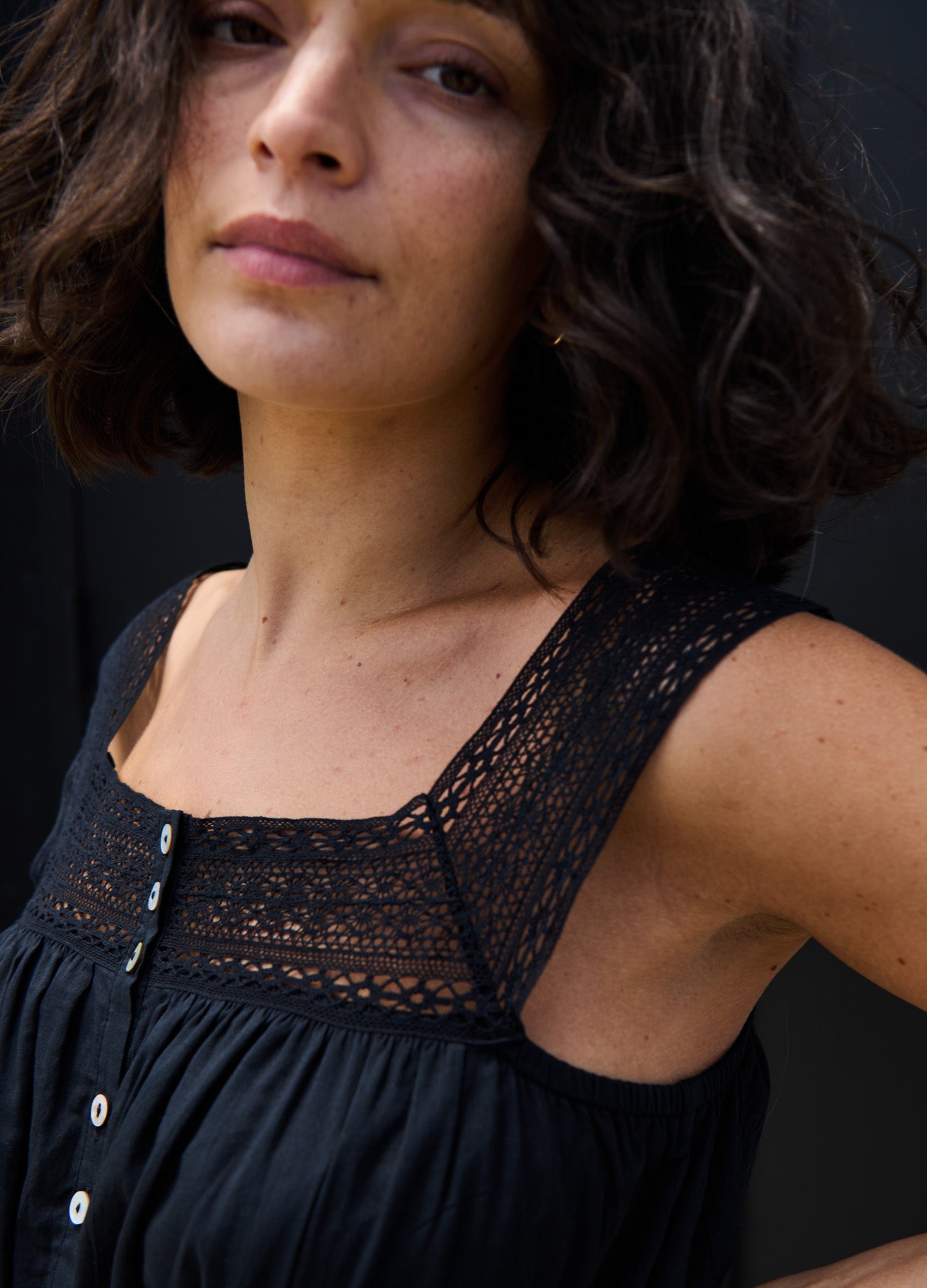 Black sleeveless maternity dress with lace square neckline and buttoned front panel.