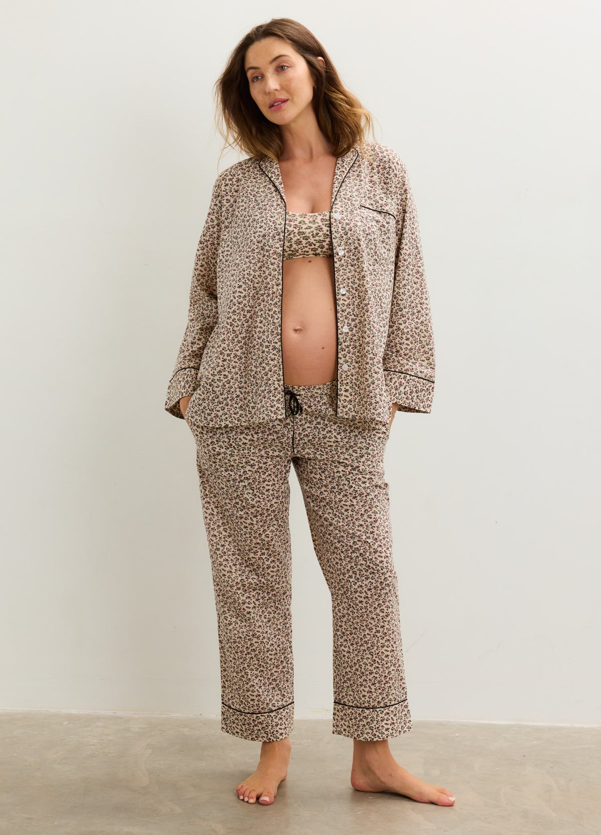Pregnant model wearing a beige floral cotton pajama set with a button-front top, nursing-friendly bra, and relaxed pants.