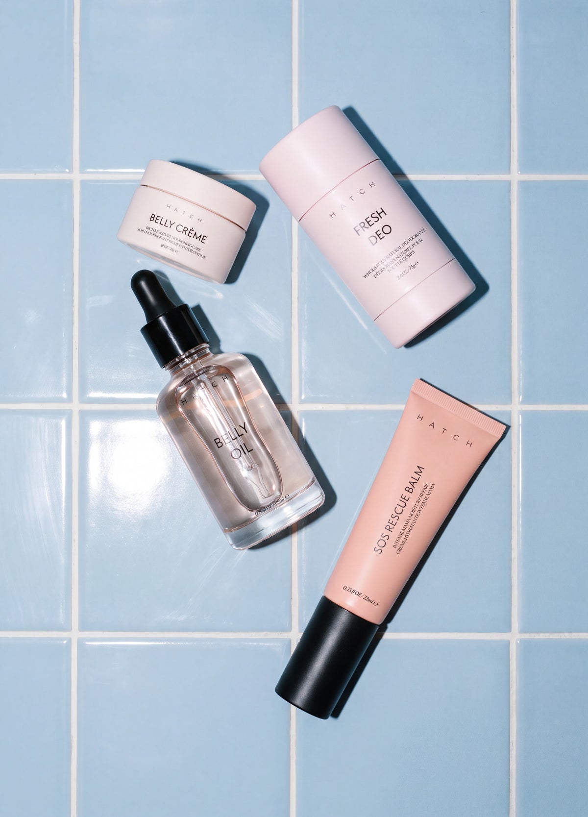 Set of four skincare products including pink cream jar, pink deodorant stick, clear dropper bottle, and pink tube on blue.