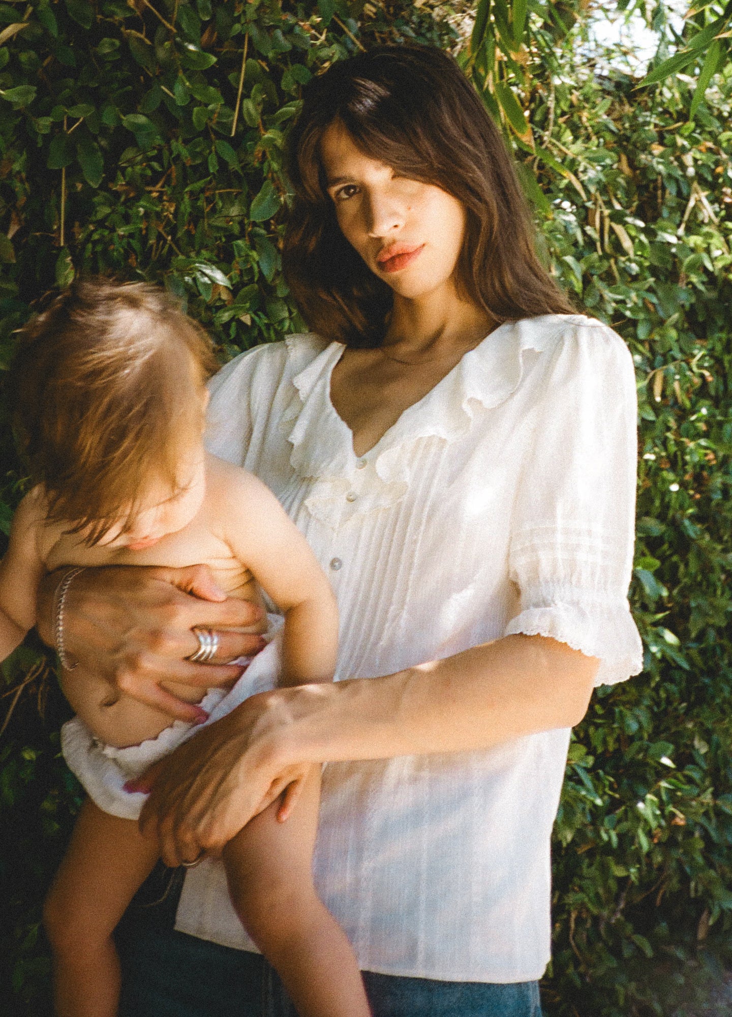 White lightweight nursing blouse with puff sleeves and button-down front worn by mother holding baby outdoors.