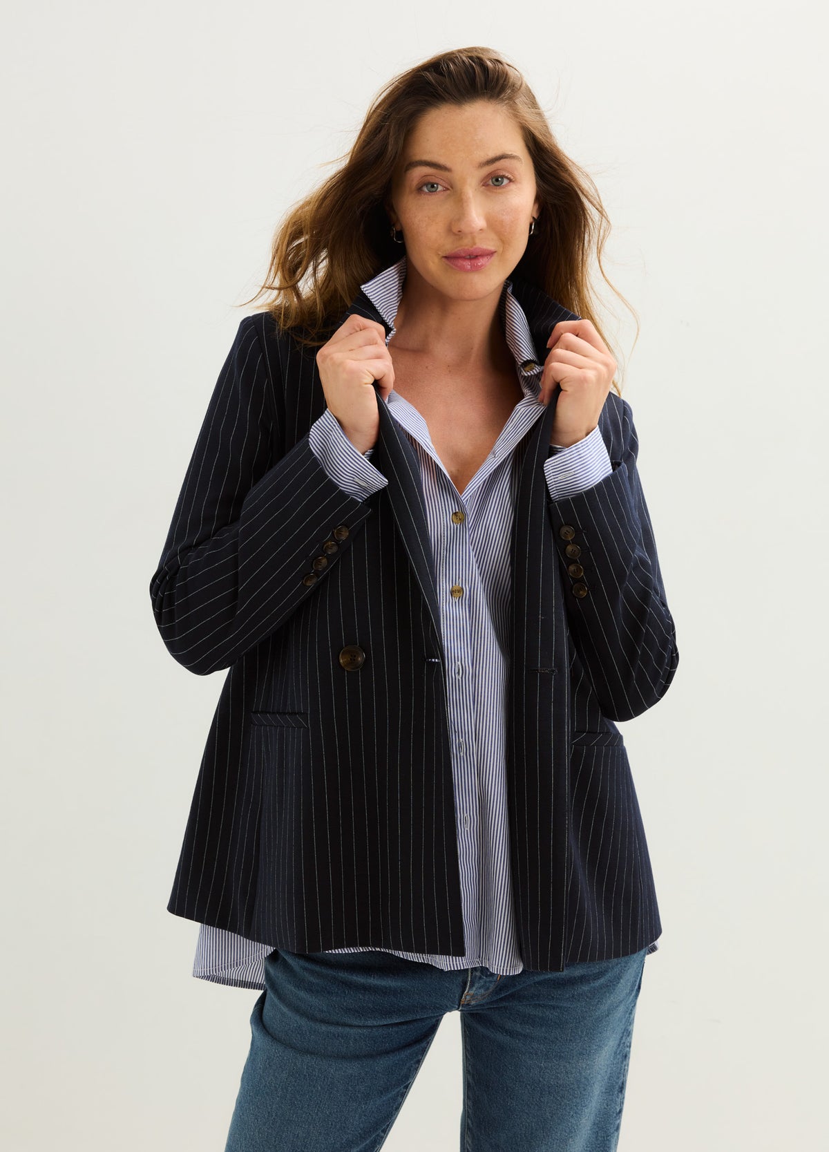 Pregnant model wearing a black pinstripe maternity blazer over a pale blue shirt and jeans.