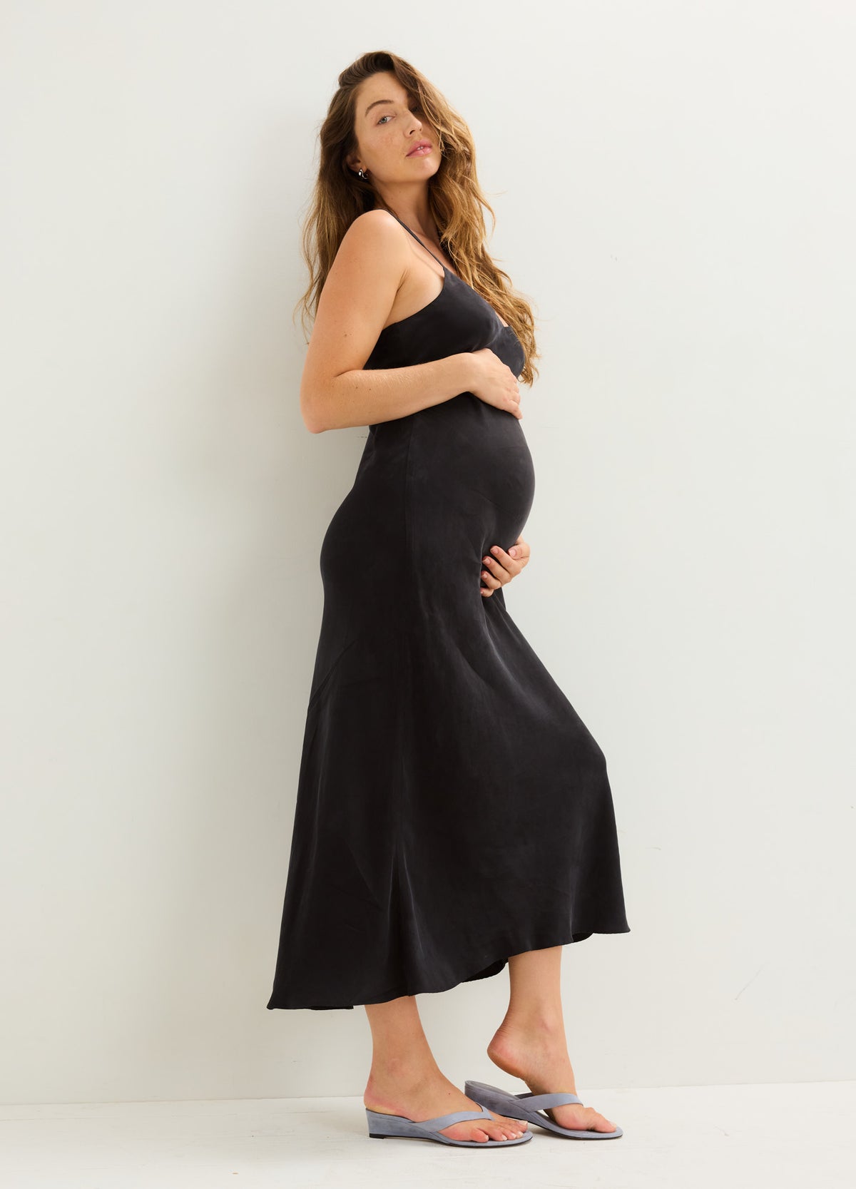 Black satin slip dress with thin straps, midi length, worn by pregnant model.