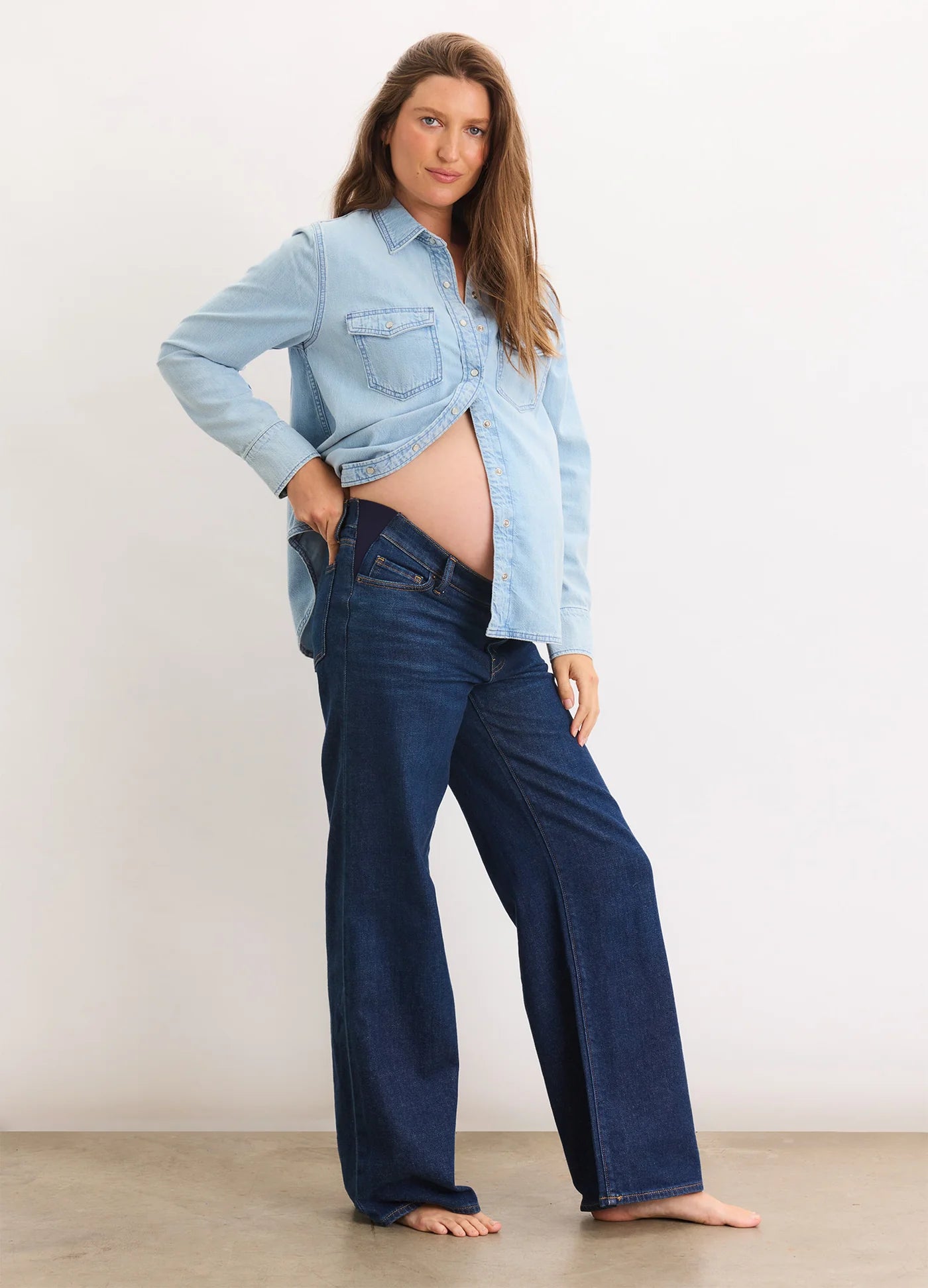 Dark blue wide-leg maternity jeans with a relaxed fit worn by a pregnant model paired with a light blue button-up shirt.