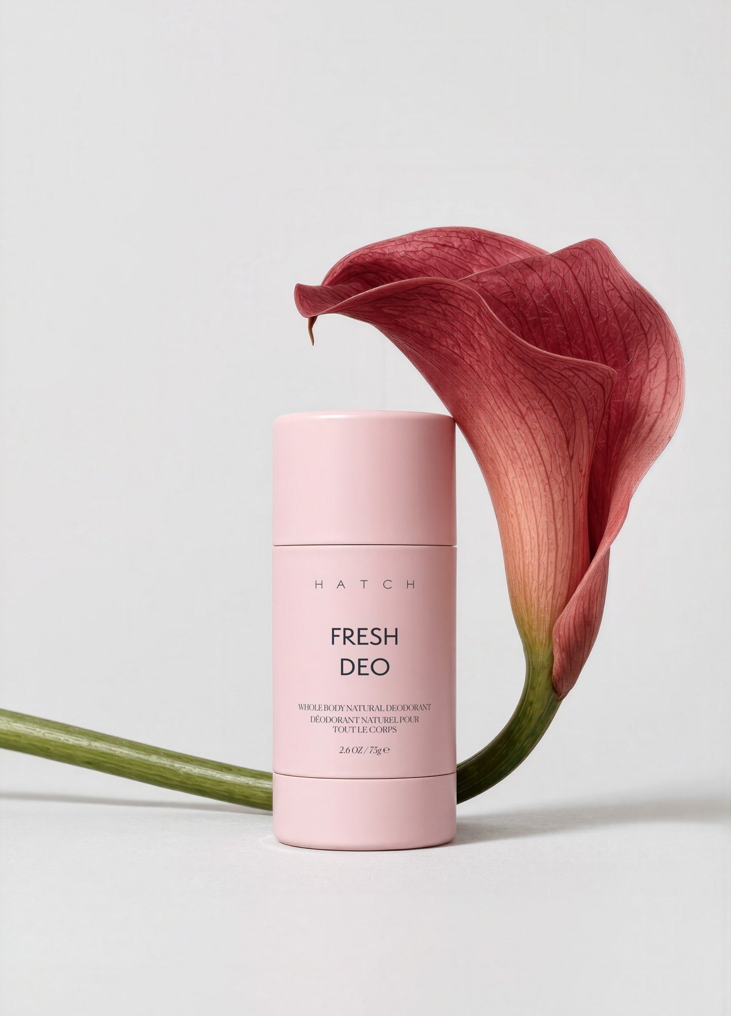 Pink cylindrical Fresh Deo stick with minimalist black text, standing next to a deep red calla lily flower.
