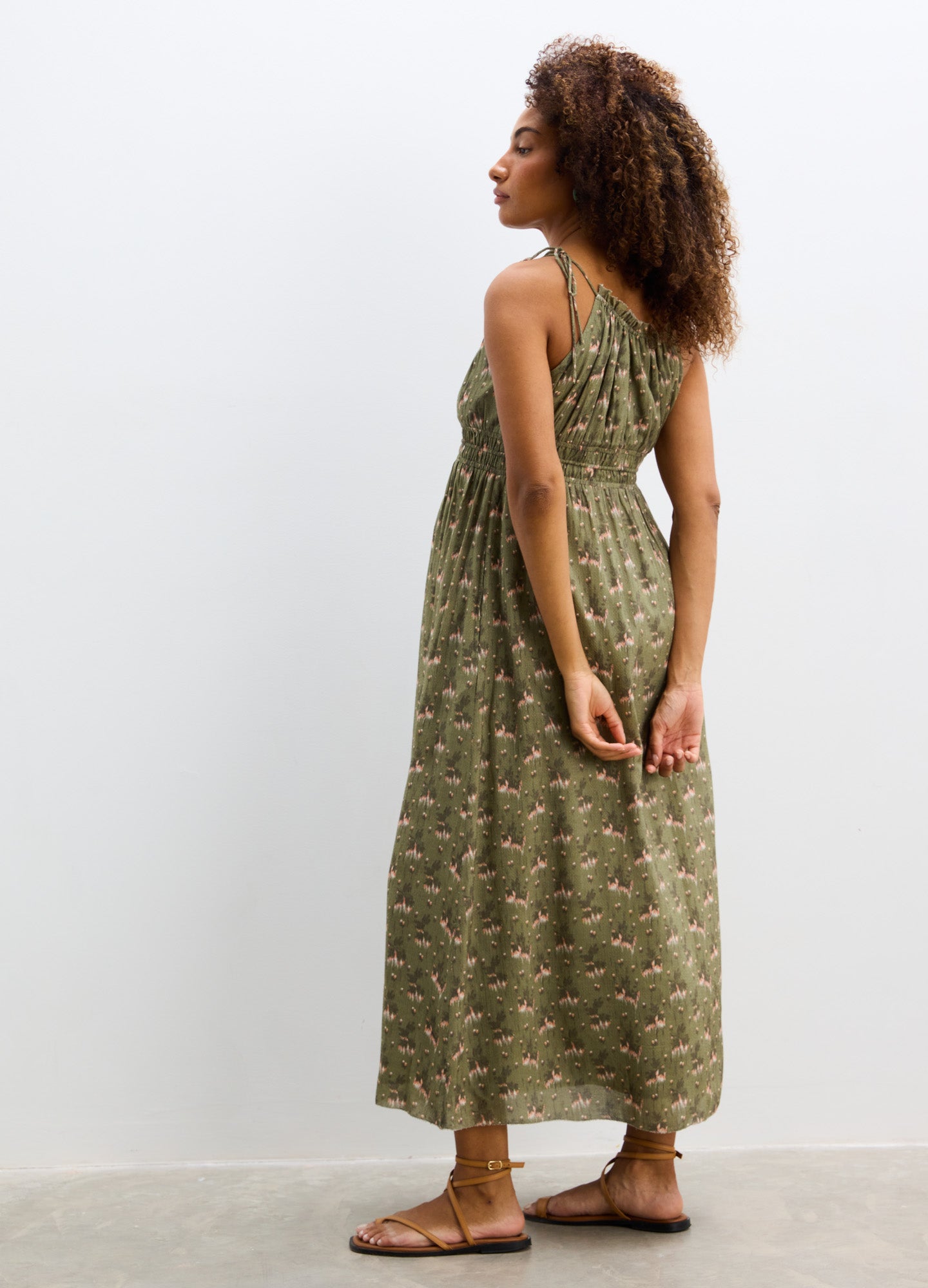 Olive green sleeveless maternity dress with small floral print, gathered empire waist, and ankle length.