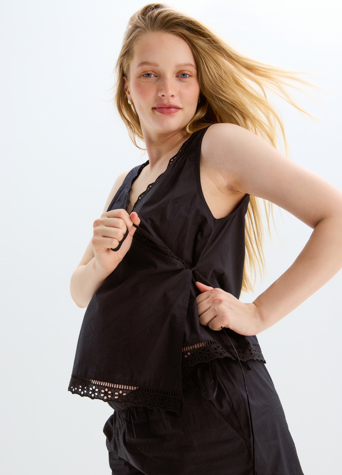 Black sleeveless maternity nursing top with zipper front and scalloped hem detail.