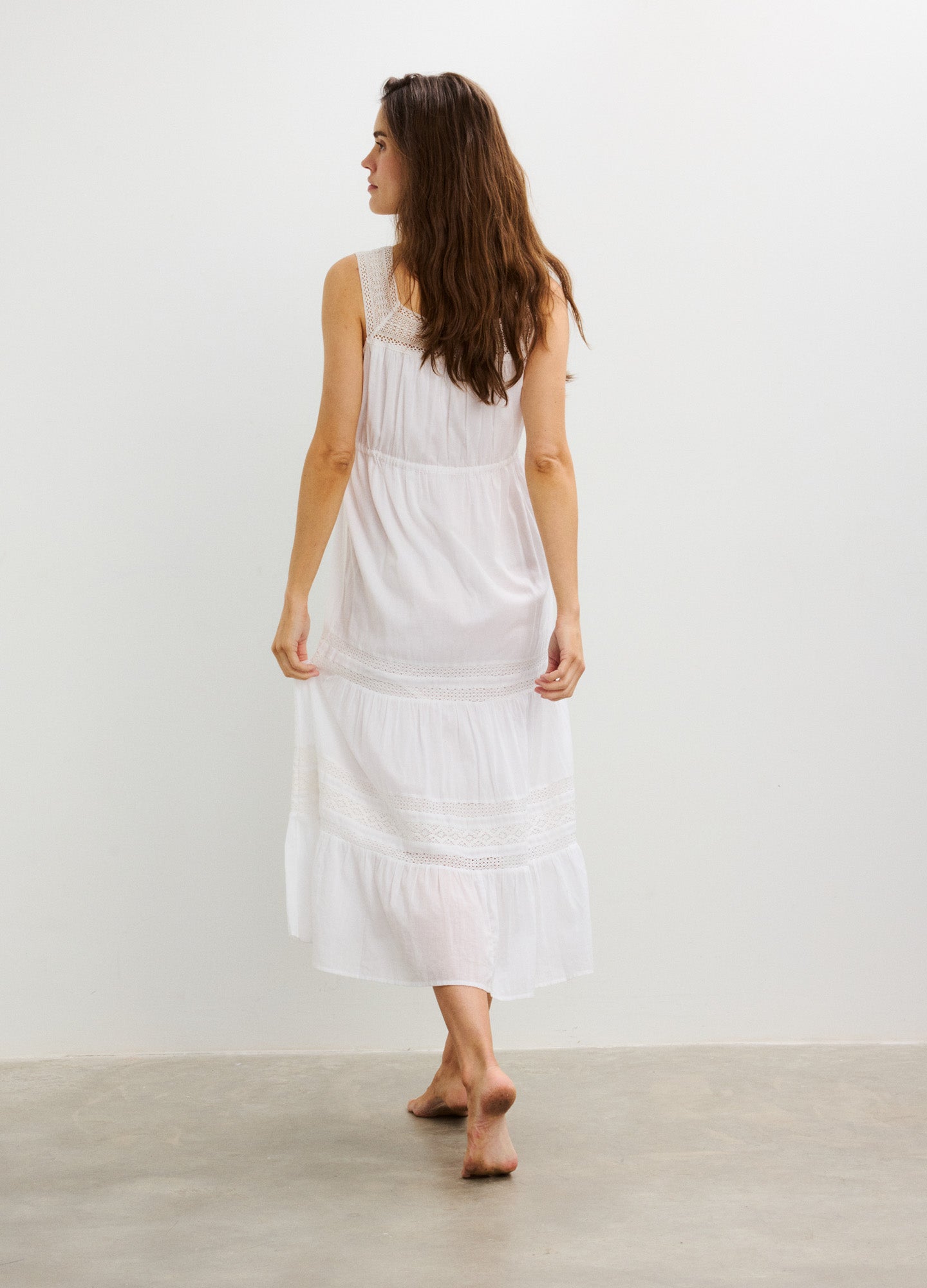 White sleeveless maternity maxi dress with tiered skirt and relaxed fit.