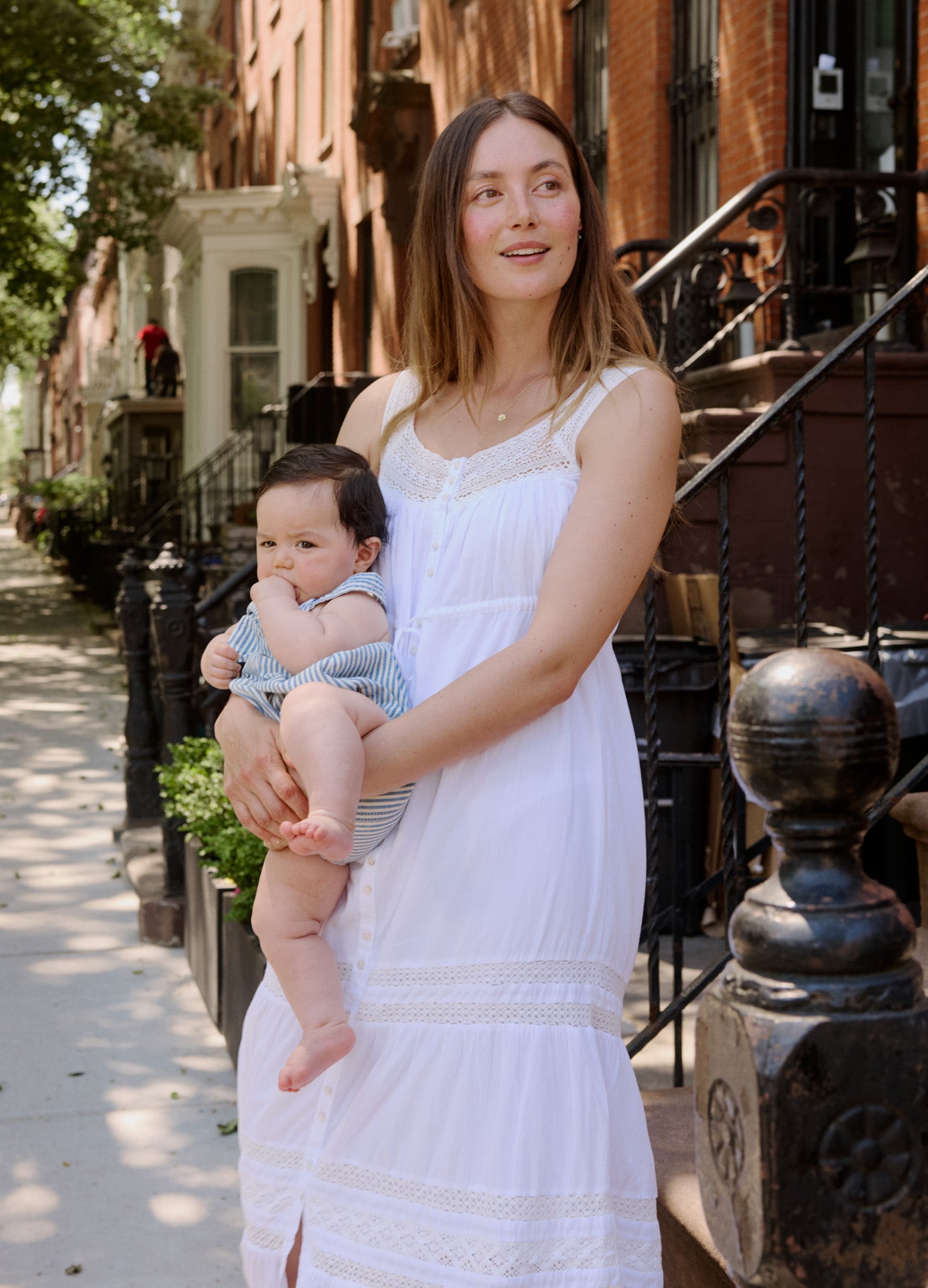 White sleeveless maternity dress with tiered skirt and smocked bodice, worn by pregnant woman outdoors.