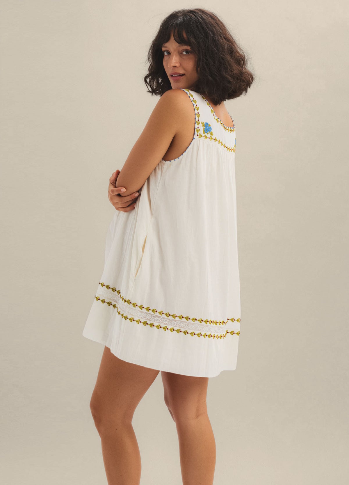 White sleeveless mini dress with loose fit and colorful embroidered trim, designed for maternity wear.