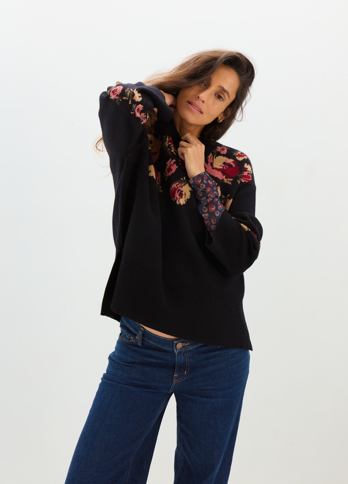 Black relaxed-fit sweater with colorful floral embroidery and blue jeans, styled for maternity wear.
