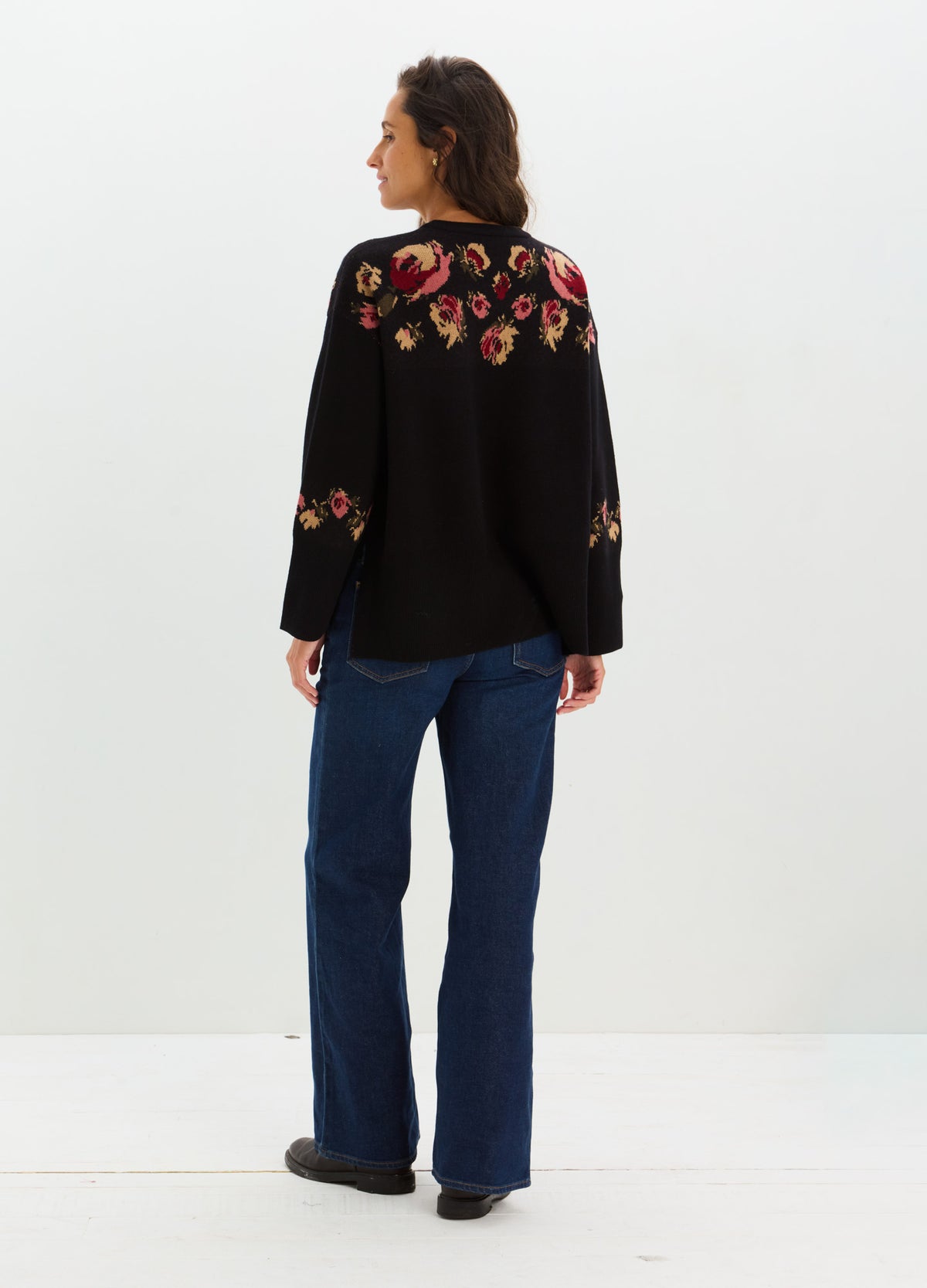 Black sweater with colorful floral embroidery across the shoulders, styled with blue jeans on a pregnant model.