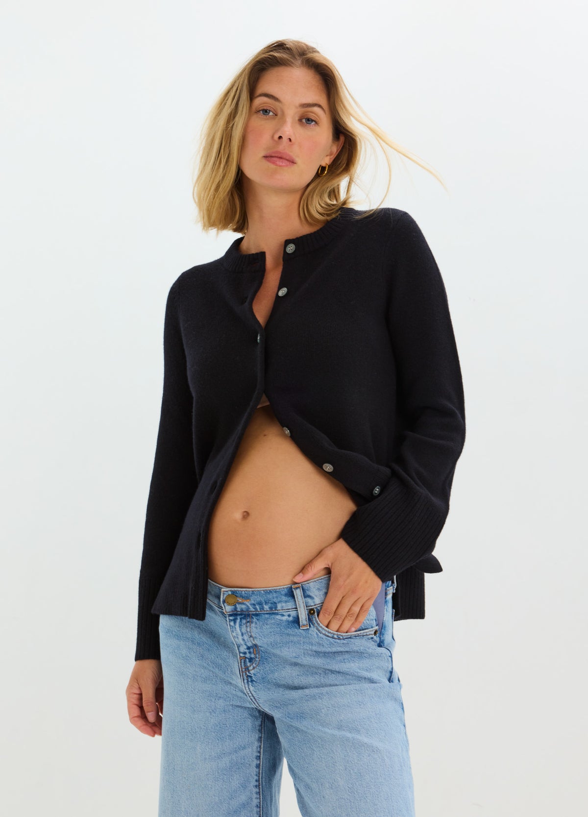 Black maternity cardigan with long sleeves and button-down front, worn open over bare belly, paired with light blue jeans.