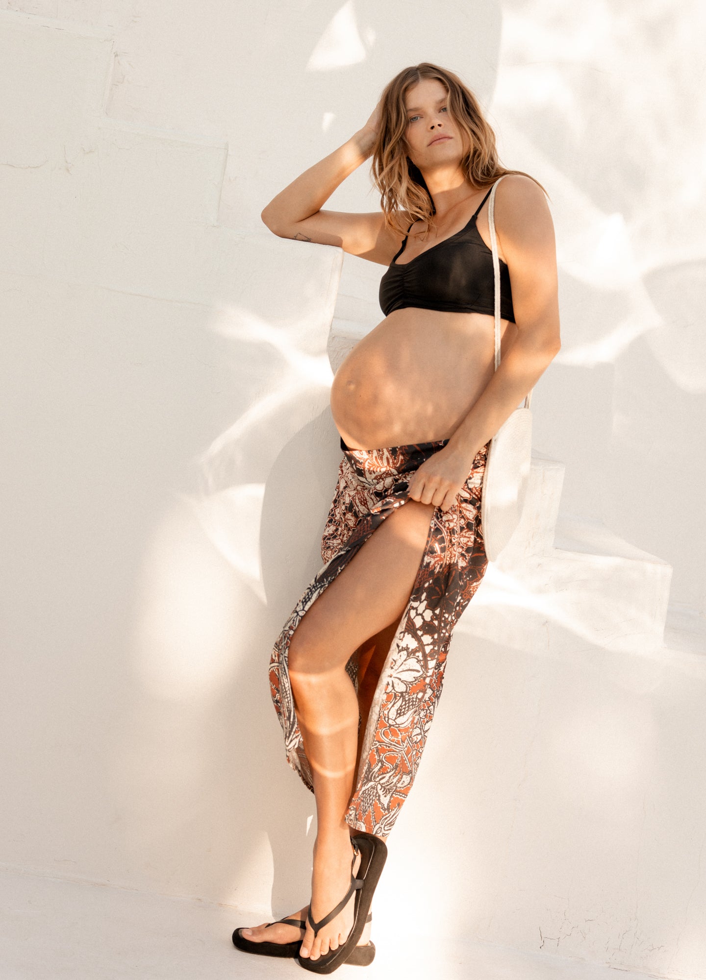 Maternity floral linen sarong with side slit, worn by pregnant woman paired with black crop top and sandals.