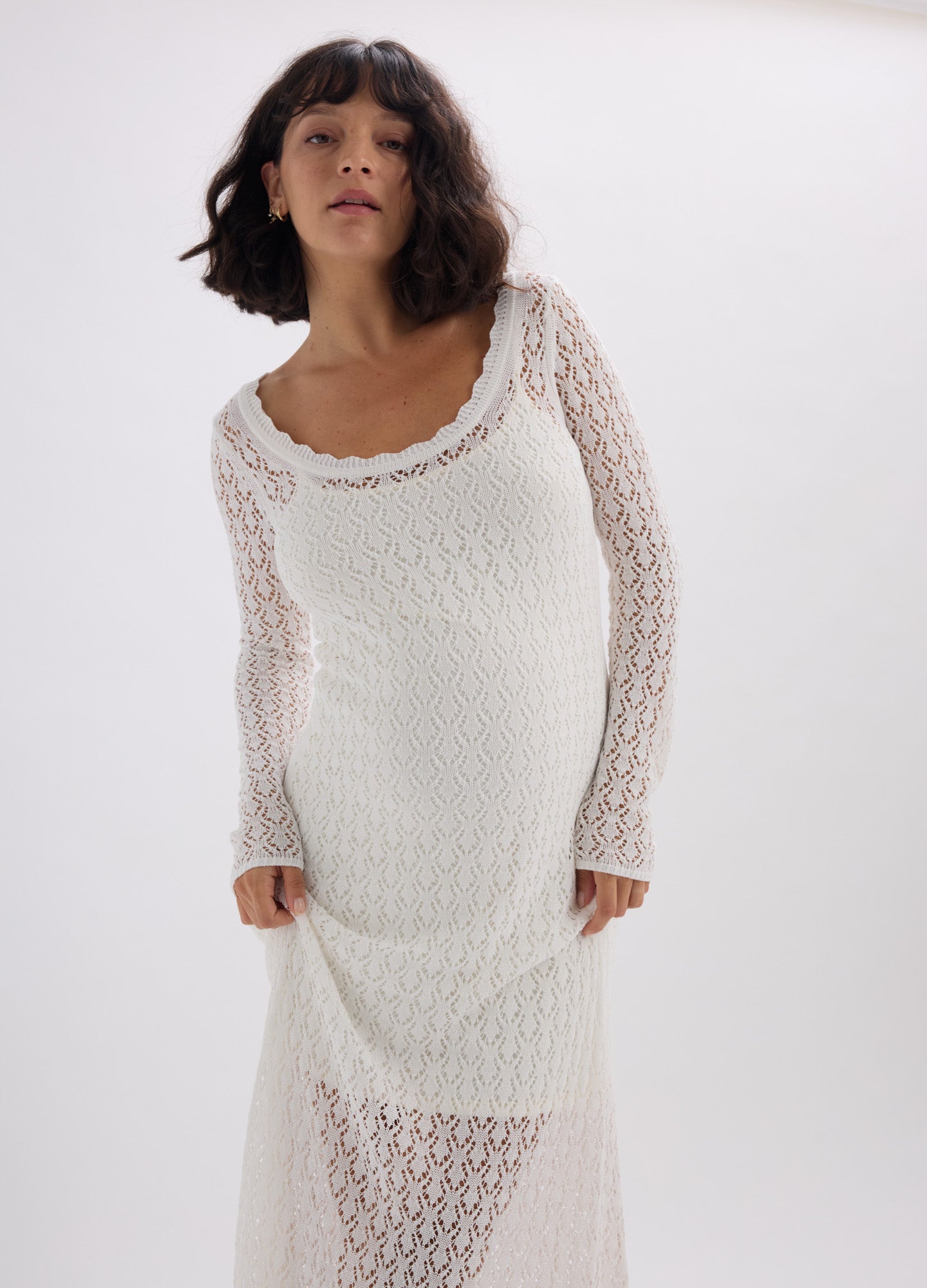 White knitted maternity dress with long sleeves and scalloped neckline, fitted for pregnant figure.