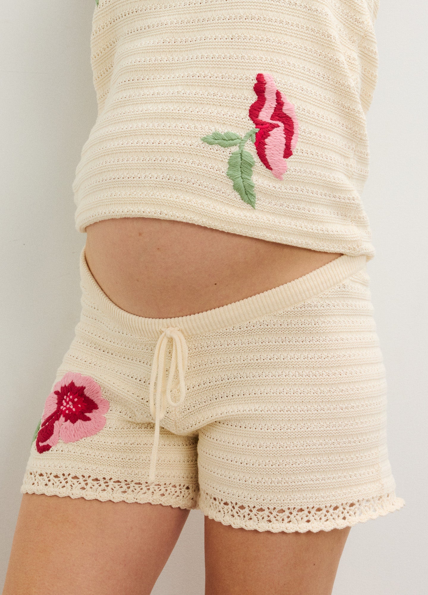 Cream ribbed maternity shorts with floral embroidery and lace trim, elastic waistband with tie.