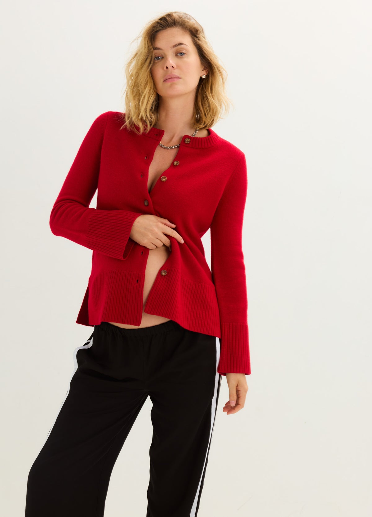 Red fitted button-front cardigan with long sleeves, worn open over a black top and trousers.