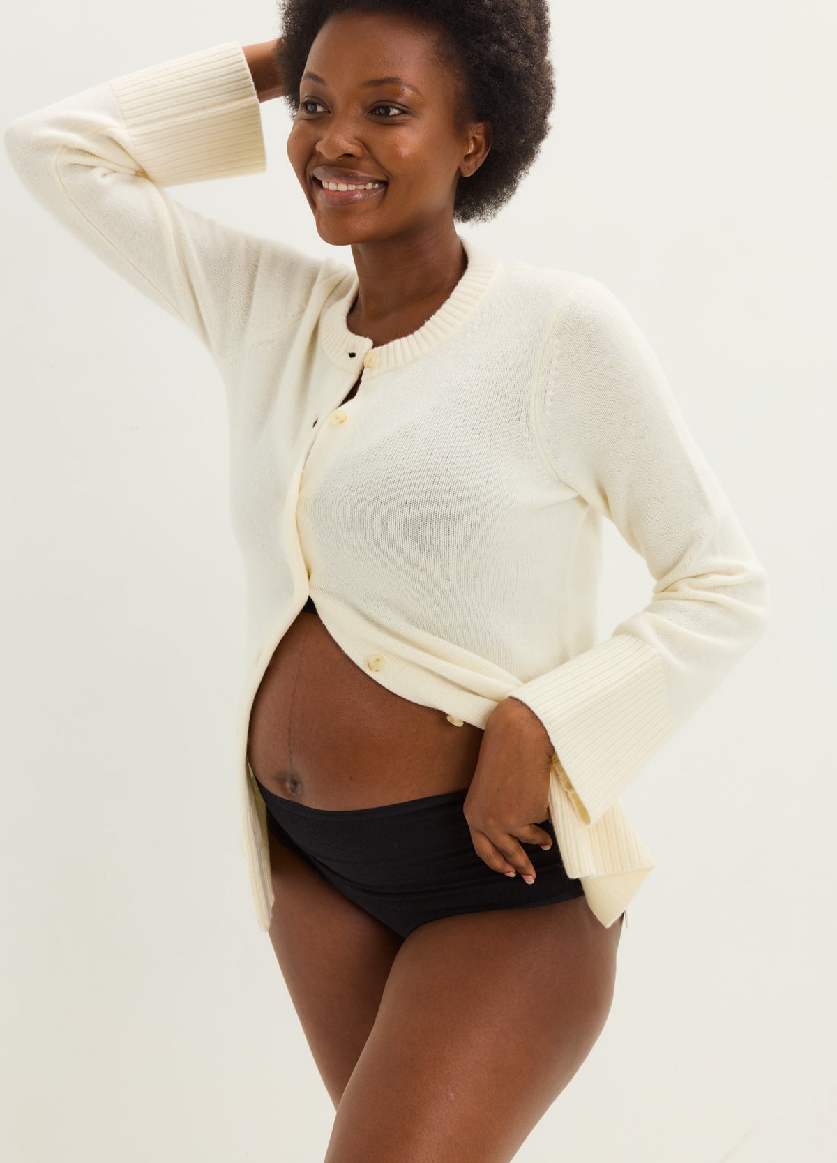 Cream knit maternity cardigan with a relaxed fit and button closure, worn open over a baby bump.