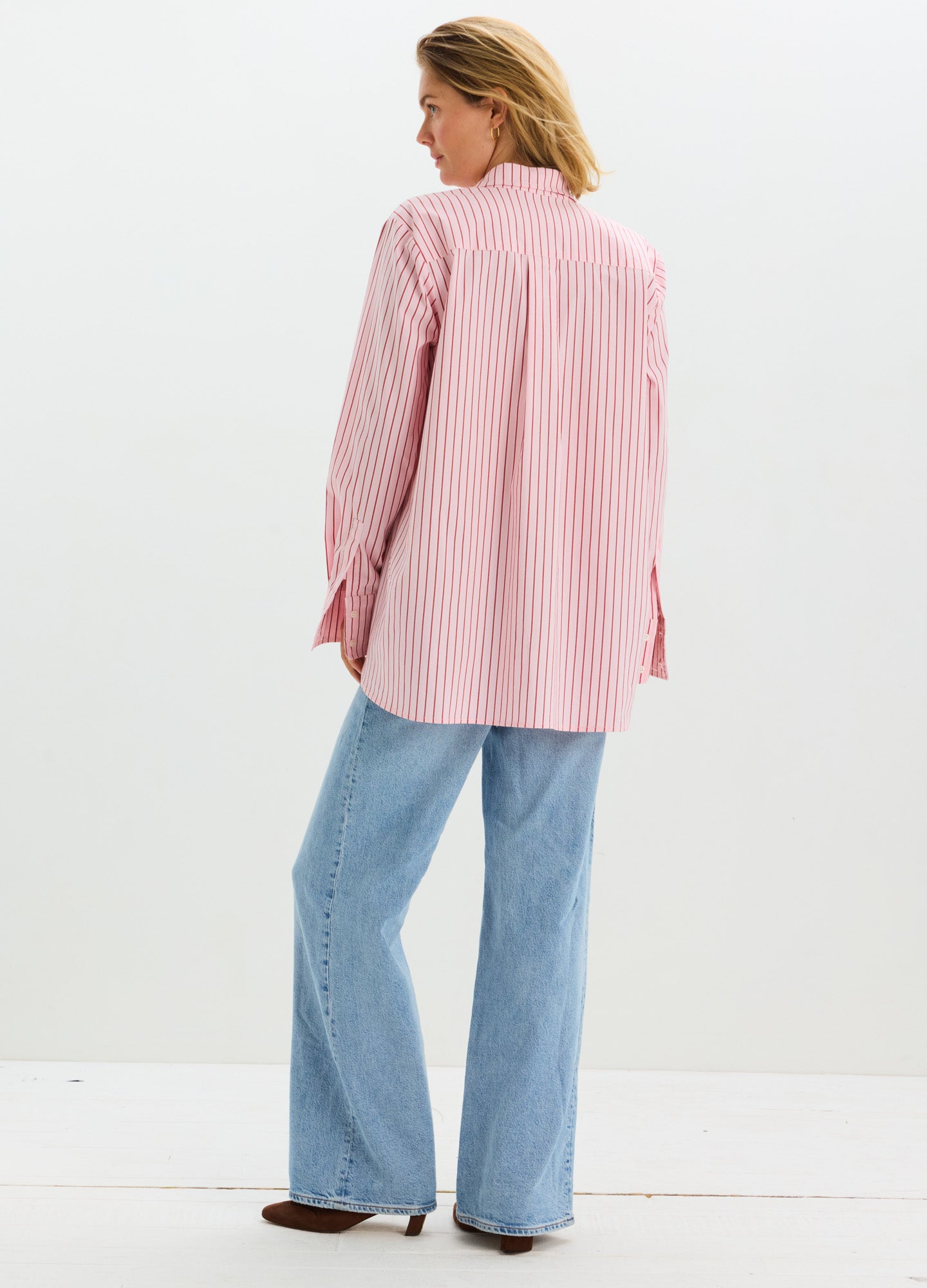 Pink and white striped long-sleeve maternity buttondown shirt with a relaxed fit, worn with light blue jeans.