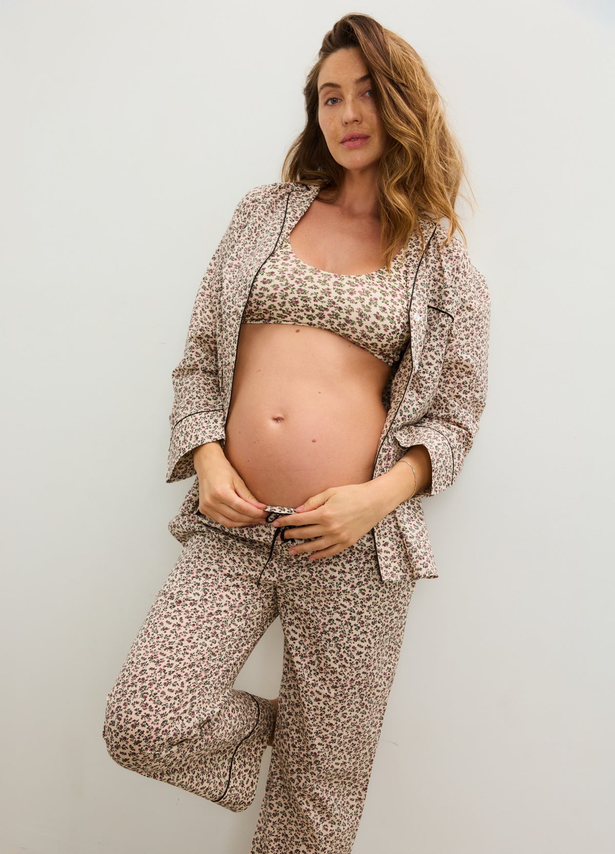 Pregnant model wearing a cream cotton maternity pajama set with a tiny floral print, cropped top, and relaxed button-front.