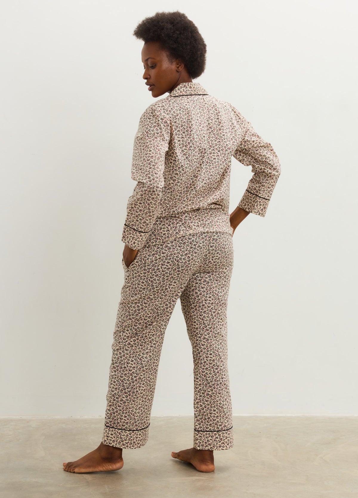Pregnant model wearing a beige cotton maternity pajama set with a small brown print, button-up top, and relaxed pants.