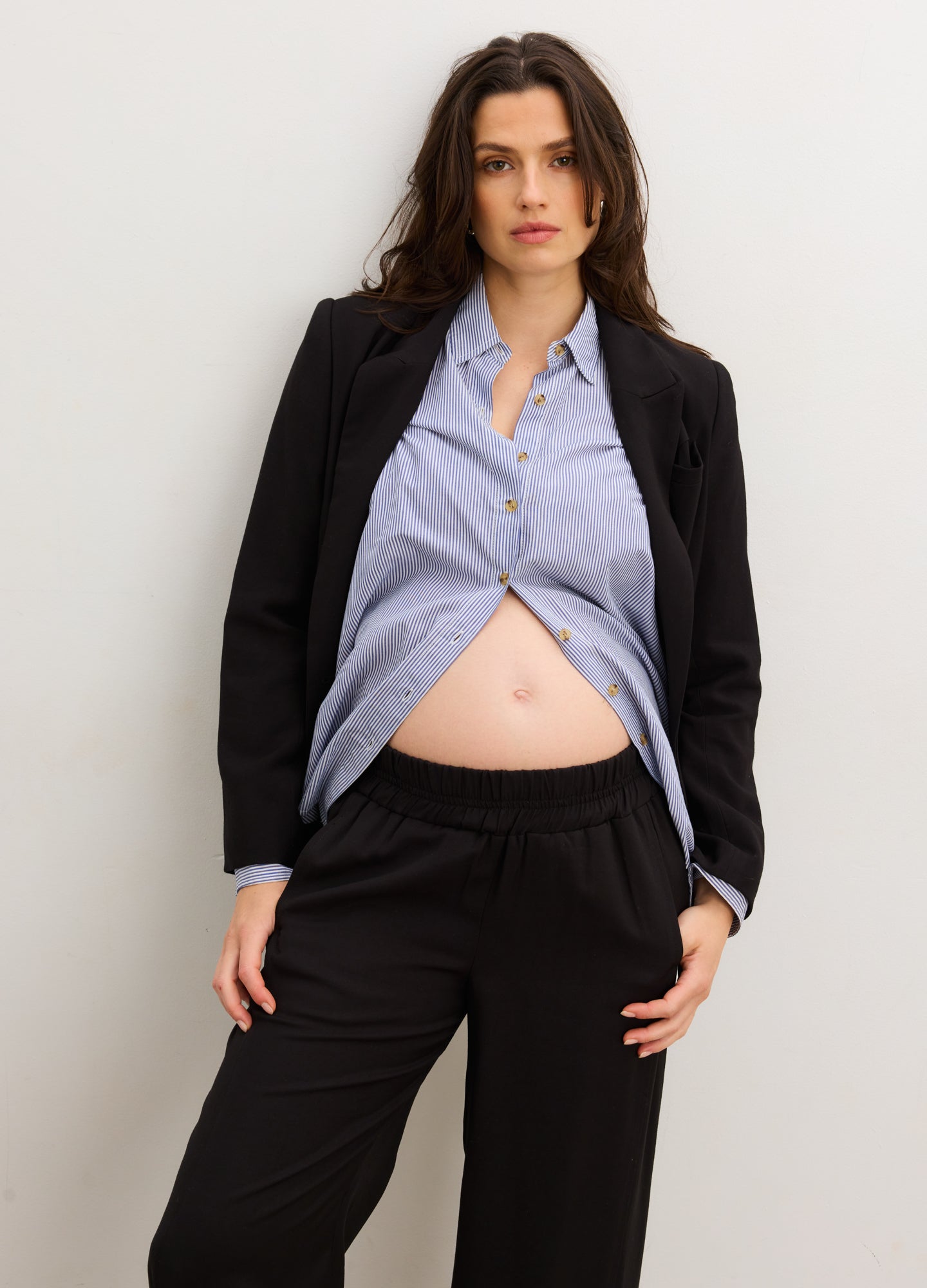 Light blue maternity buttondown shirt with long sleeves, worn open under black blazer and paired with black pants.
