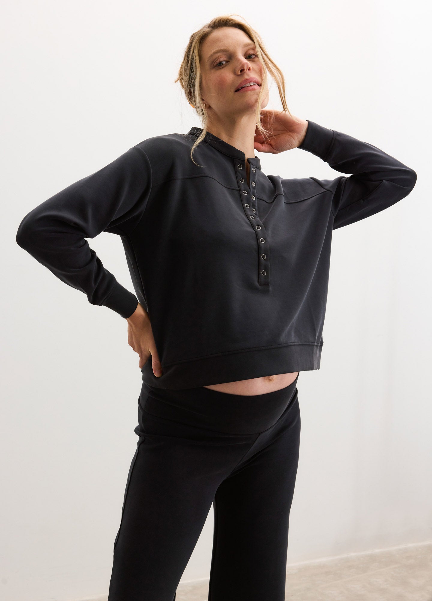 Black maternity pullover with buttoned collar and relaxed fit, styled for pregnant comfort.