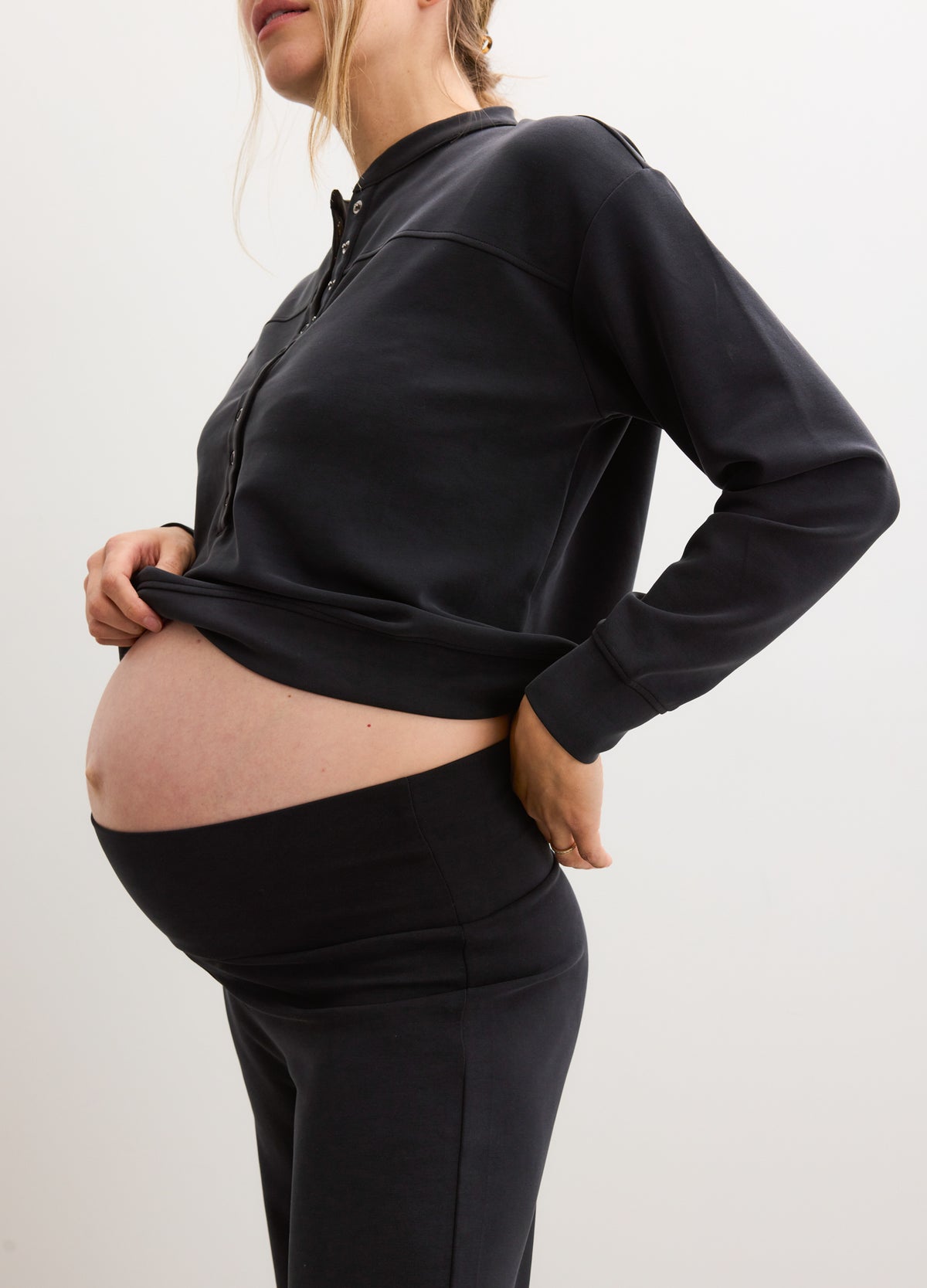 Black maternity pullover with high collar and relaxed fit, worn over a pregnant belly.