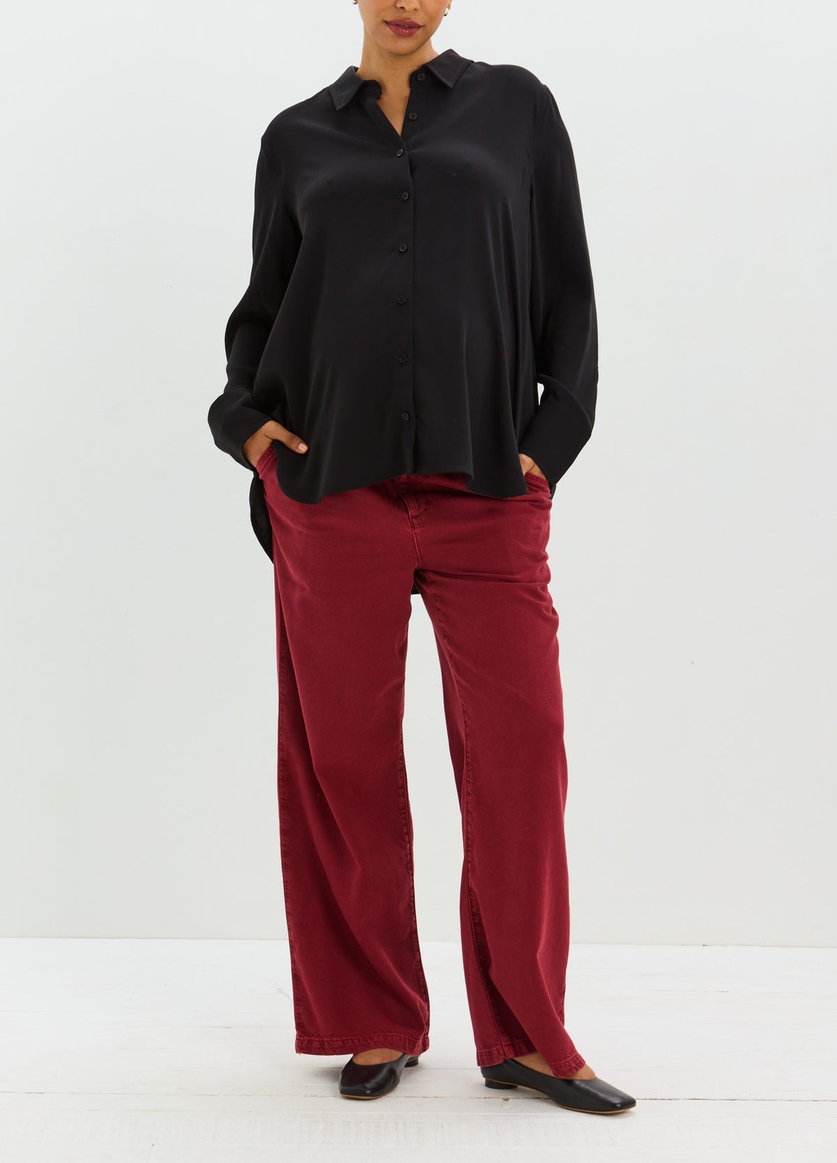 Relaxed black button-down shirt with long sleeves, paired with straight-leg burgundy trousers.