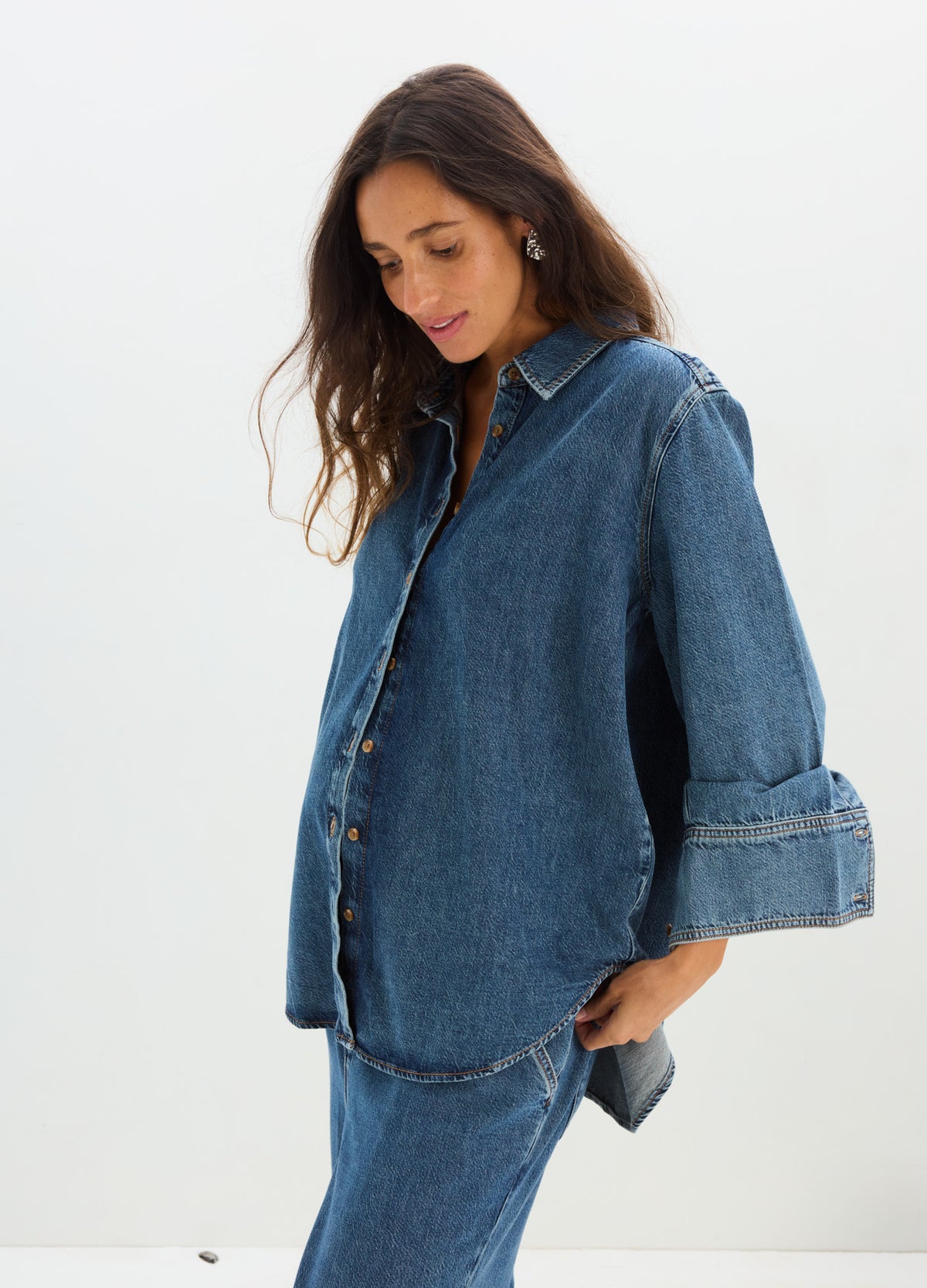 Loose-fitting dark blue denim boyfriend shirt with button front and wide rolled-up sleeves, styled for maternity wear.