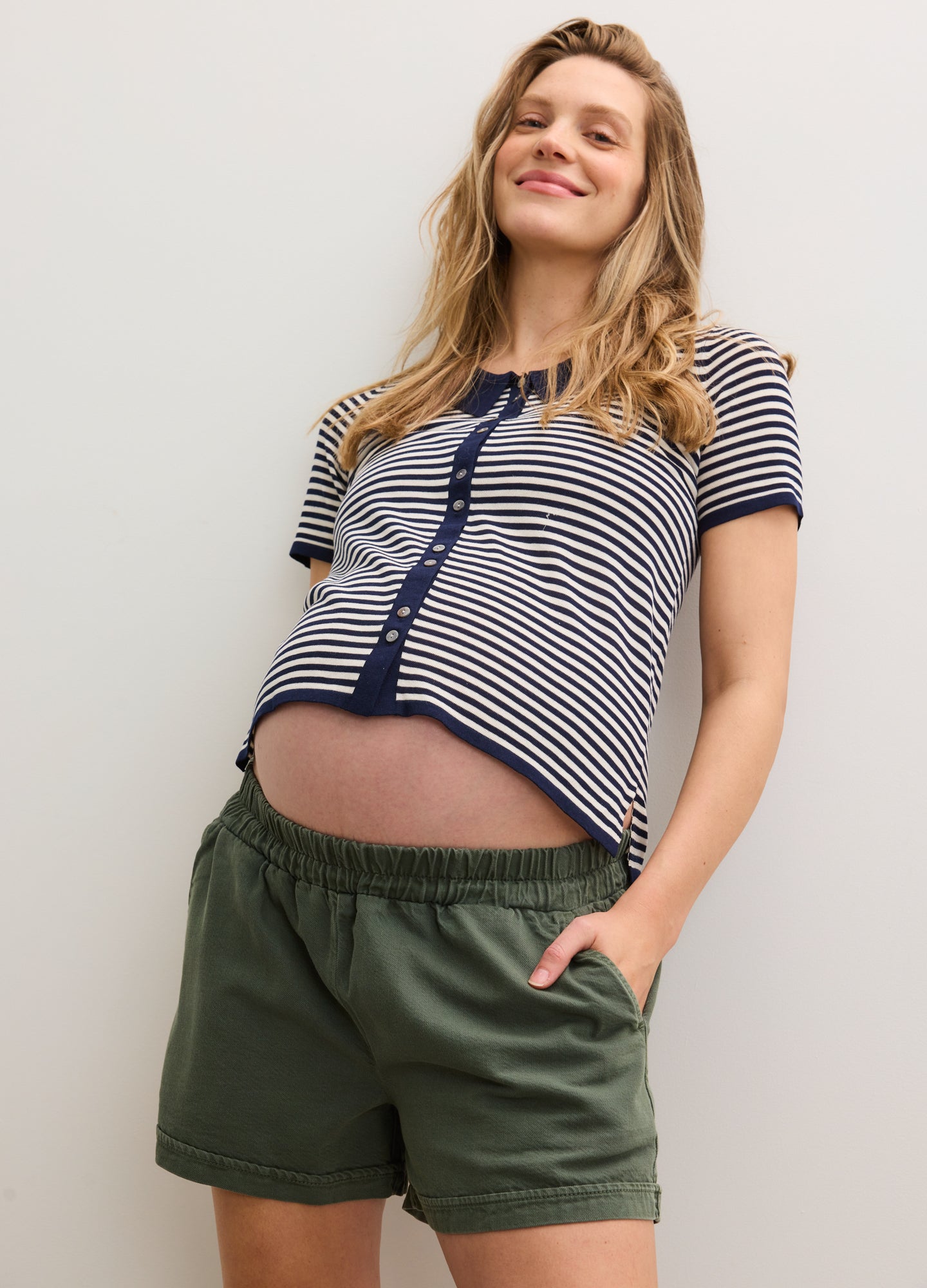 Maternity olive green drapey shorts with elastic waist, worn by smiling pregnant woman in striped navy and white top.