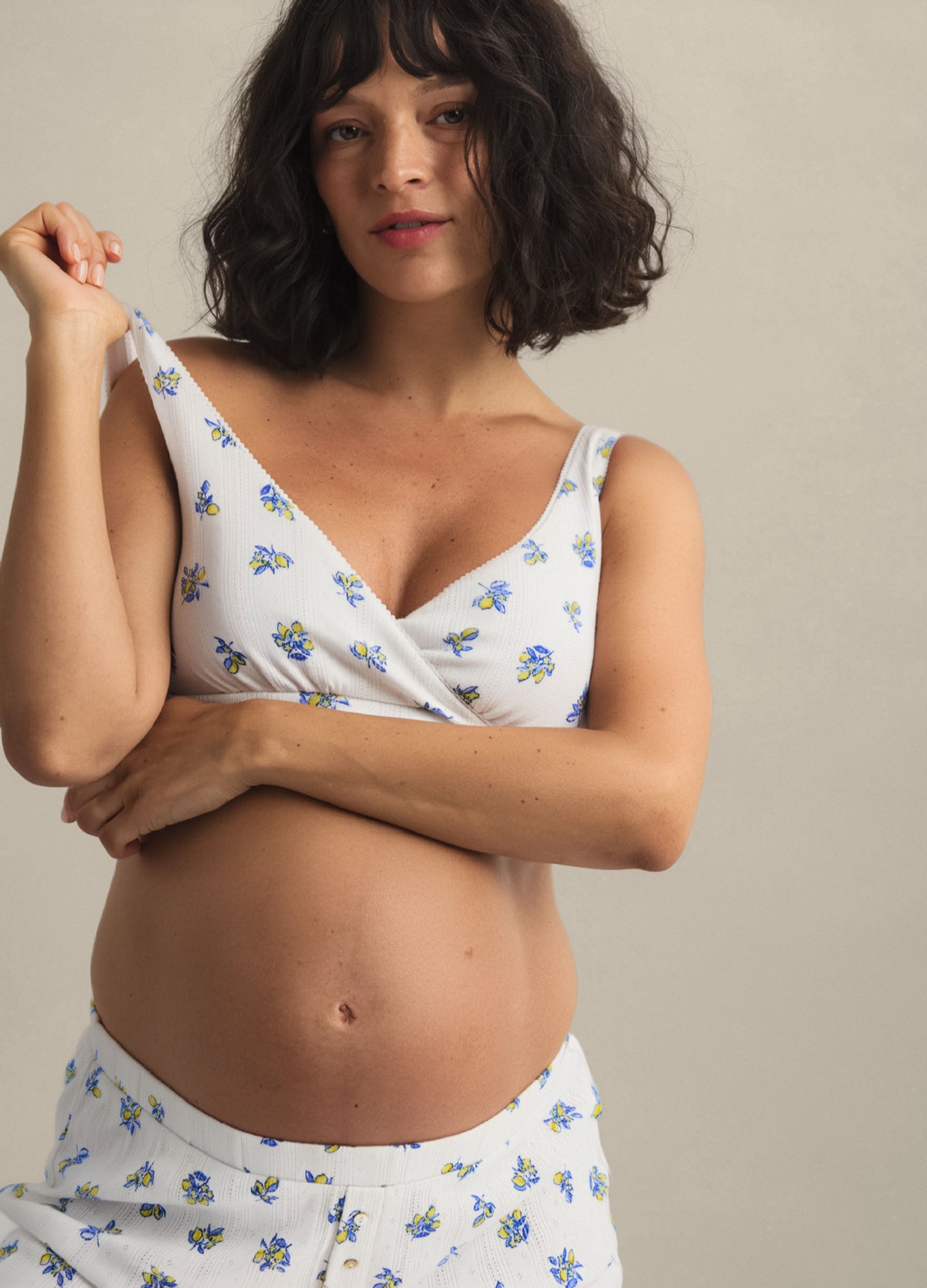 White maternity nursing bra with small blue and yellow floral print and adjustable straps on pregnant woman.