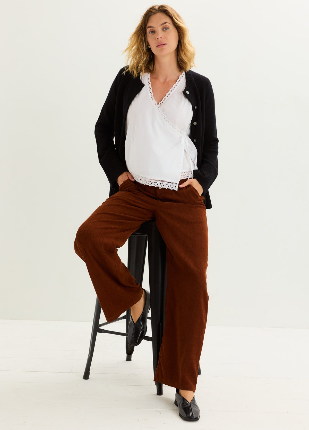 Pregnant model wearing chestnut corduroy maternity trousers with a relaxed fit and straight legs.