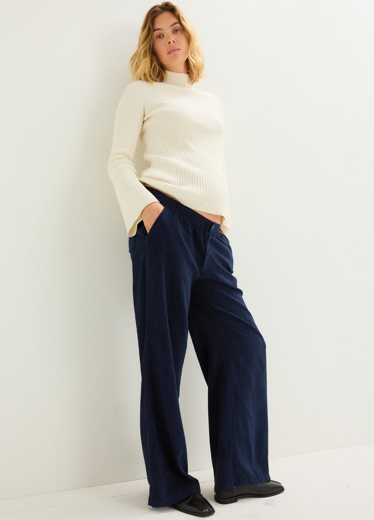 Pregnant model wearing navy maternity corduroy pants with a relaxed, wide-leg fit and pockets.