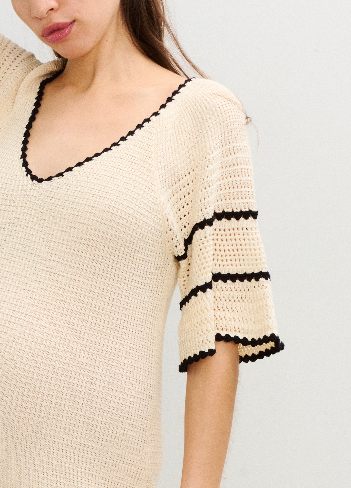 Cream-colored crochet maternity dress with black trim, V-neck and flutter sleeves.