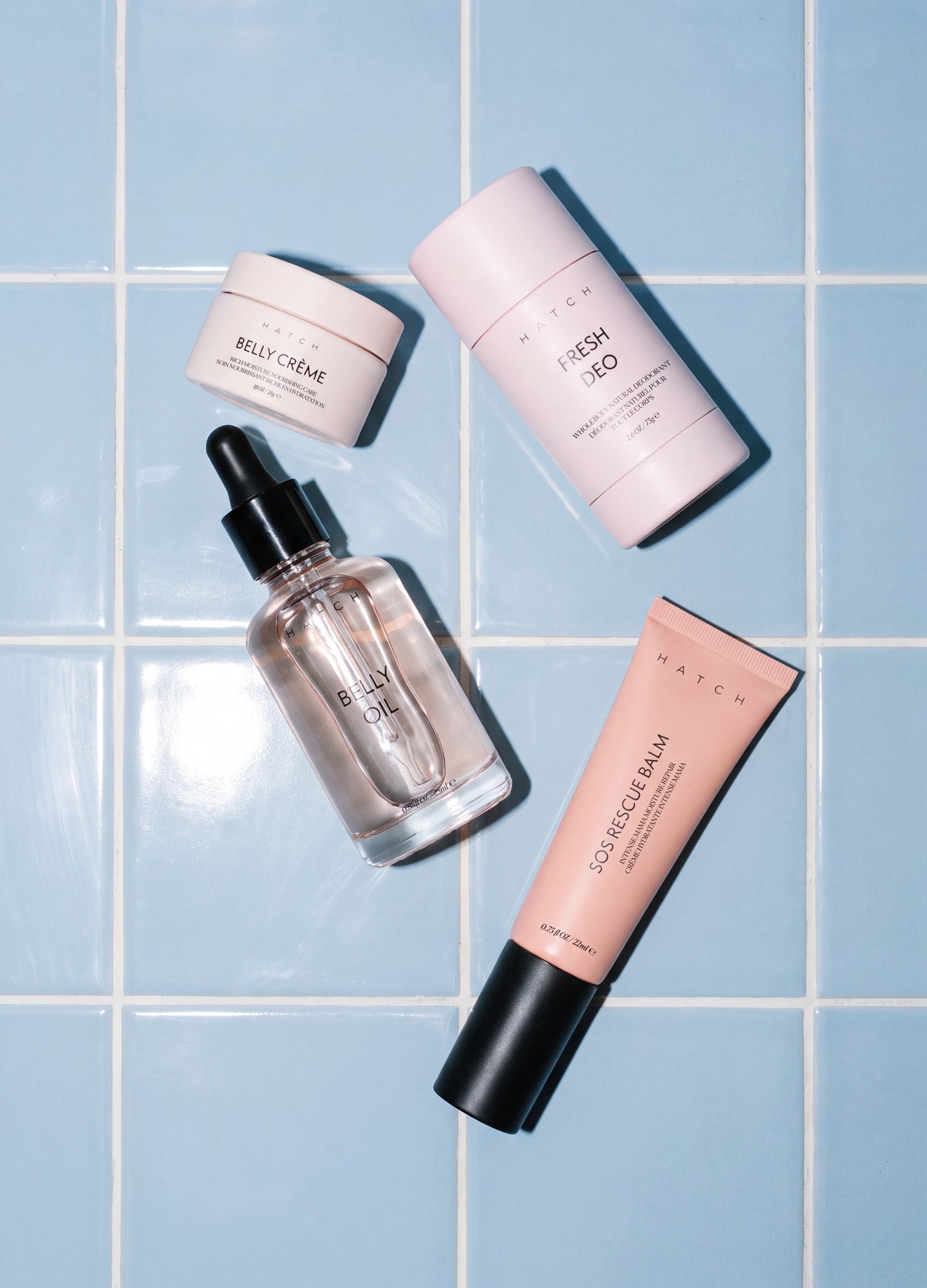 Set of four skincare products including pink cream jar, pink deodorant stick, clear dropper bottle, and pink tube on blue.
