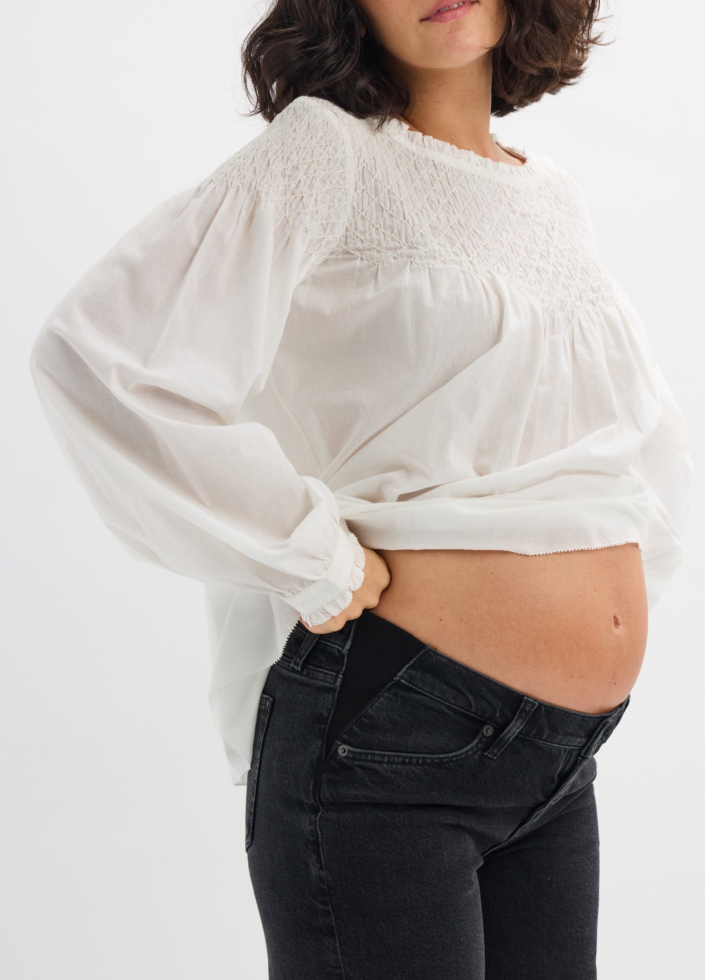 White long-sleeve maternity top with smocked yoke and loose, flowing fabric around the belly.
