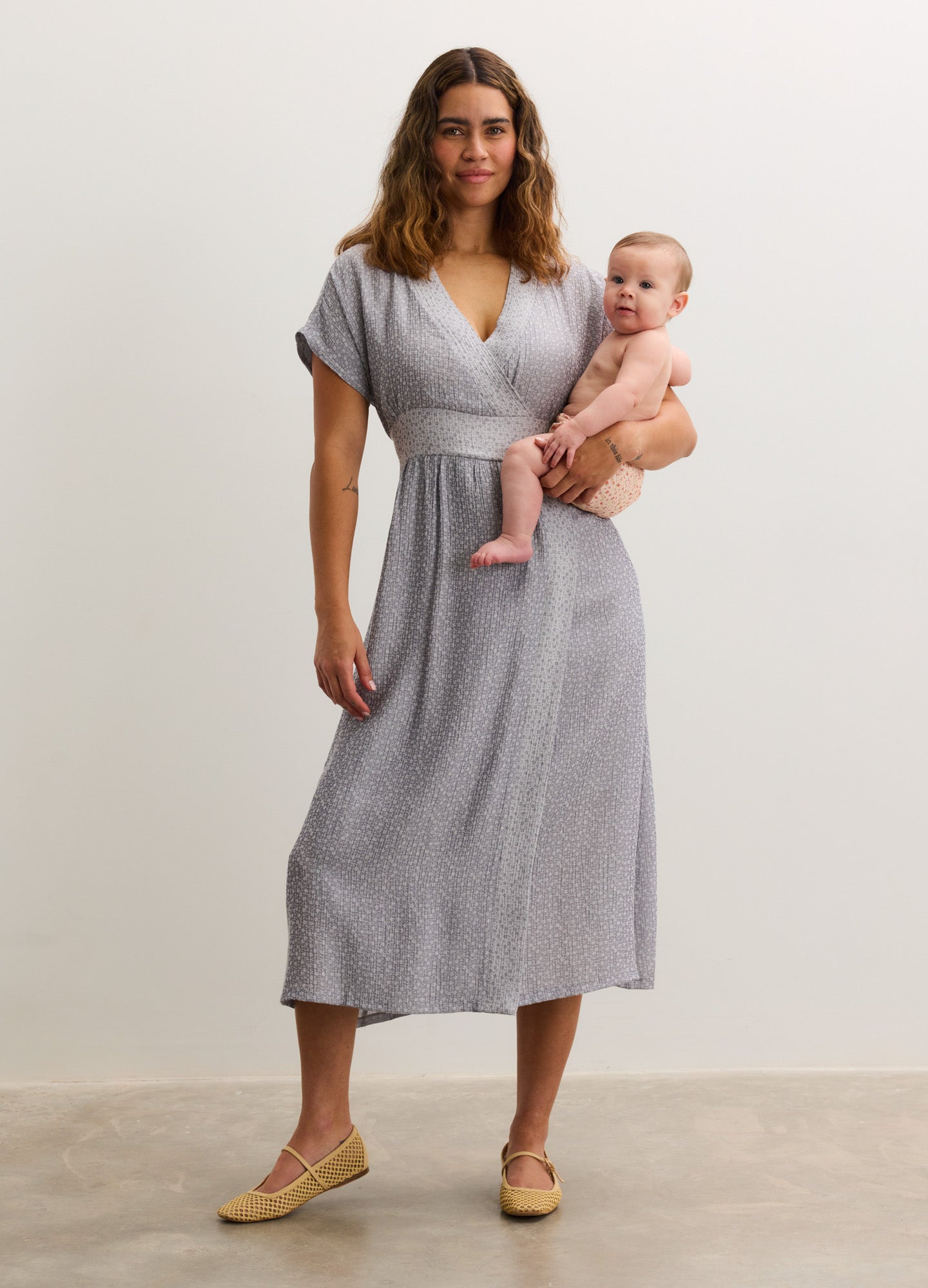 Light gray maternity midi dress with short sleeves, V-neck, and cinched waist, modeled by a pregnant woman holding a baby.