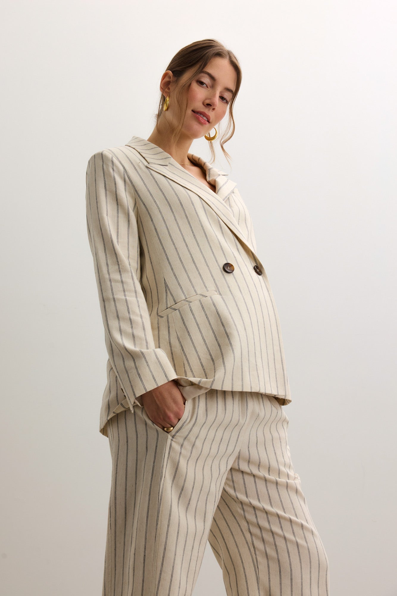 Cream-colored tailored twill blazer with thin vertical stripes, designed with extra room for maternity comfort, featuring a.