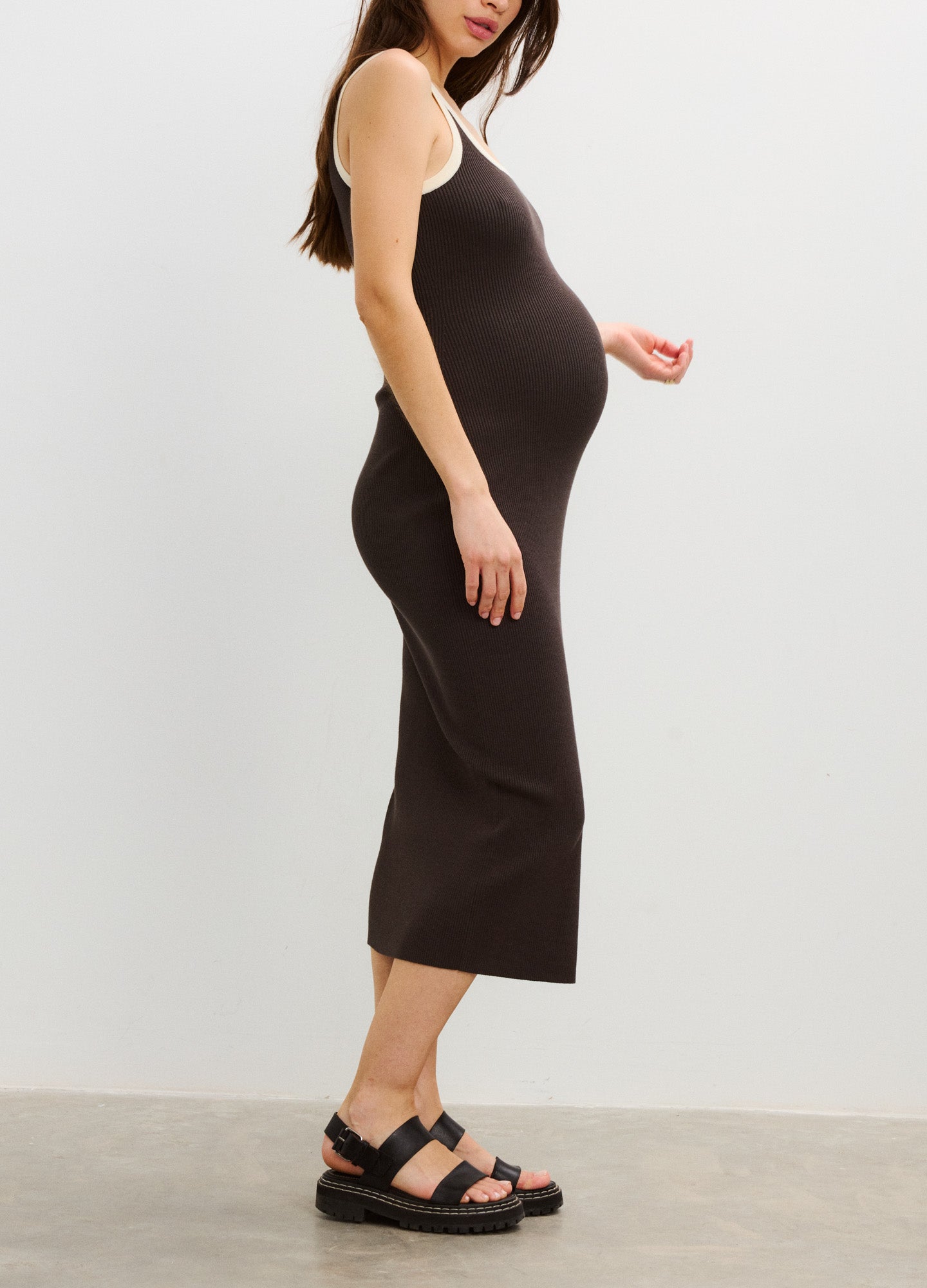 Sleeveless black midi maternity dress with scoop neckline and slim fit on pregnant model.