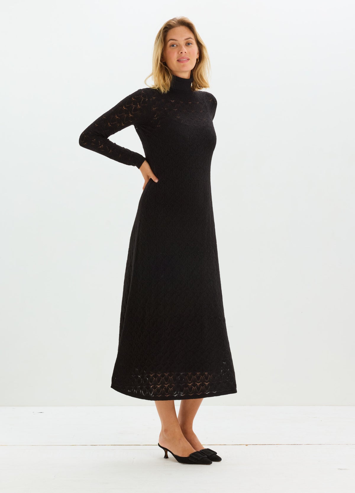 Pregnant model wearing a black long-sleeve maternity dress with a high neck and pointelle hem.