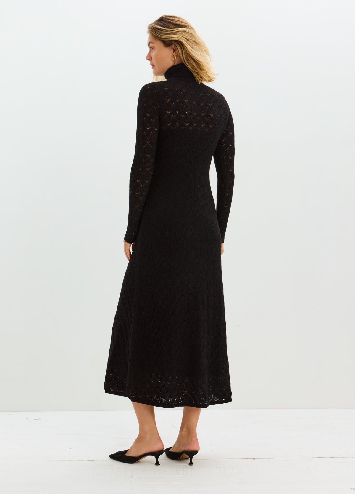 Black maternity dress with long sleeves, delicate pointelle detailing, and a flared mid-calf skirt.