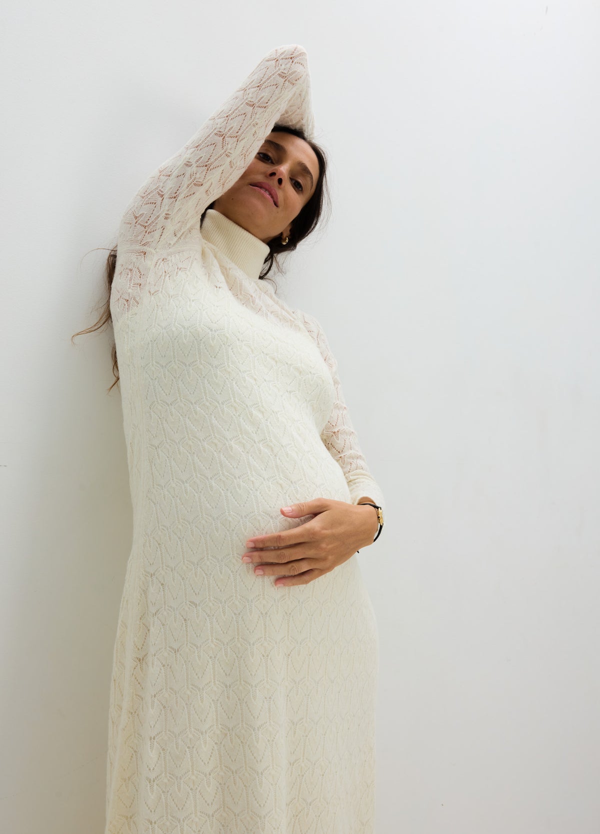 Pregnant model in an ivory long-sleeve pointelle maternity dress with a high neckline and flowing skirt.