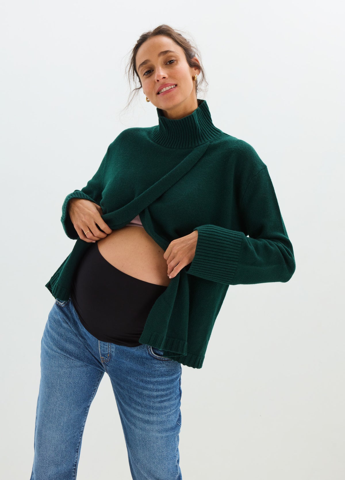 Pregnant model wearing a dark green nursing turtleneck with a front lift-up panel over a black maternity top.