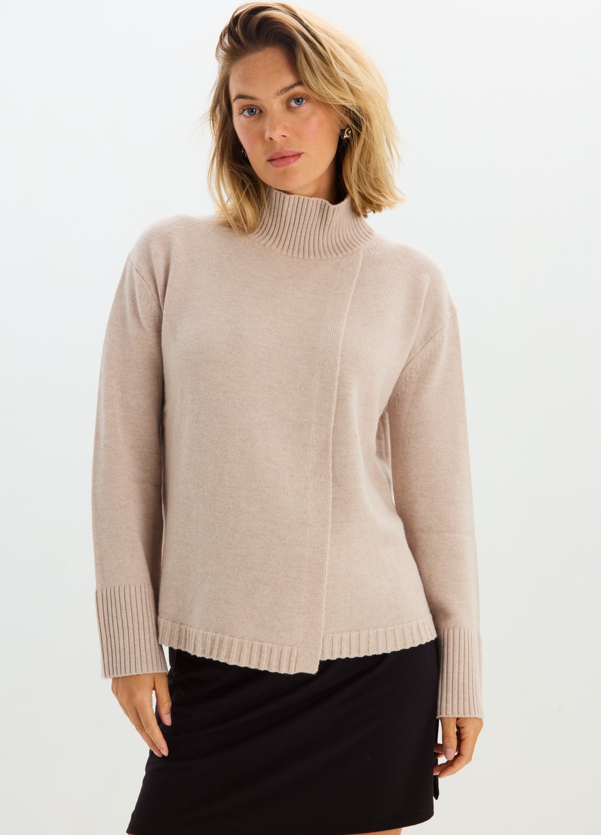 Pregnant model wearing a soft beige maternity nursing turtleneck with long sleeves and ribbed hem.