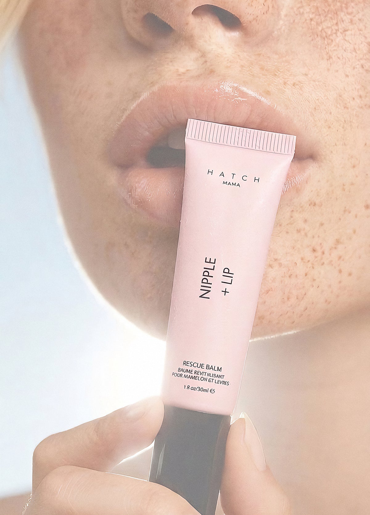 Soft pink tube of Nipple + Lip balm with black cap held near lips, smooth creamy texture visible.