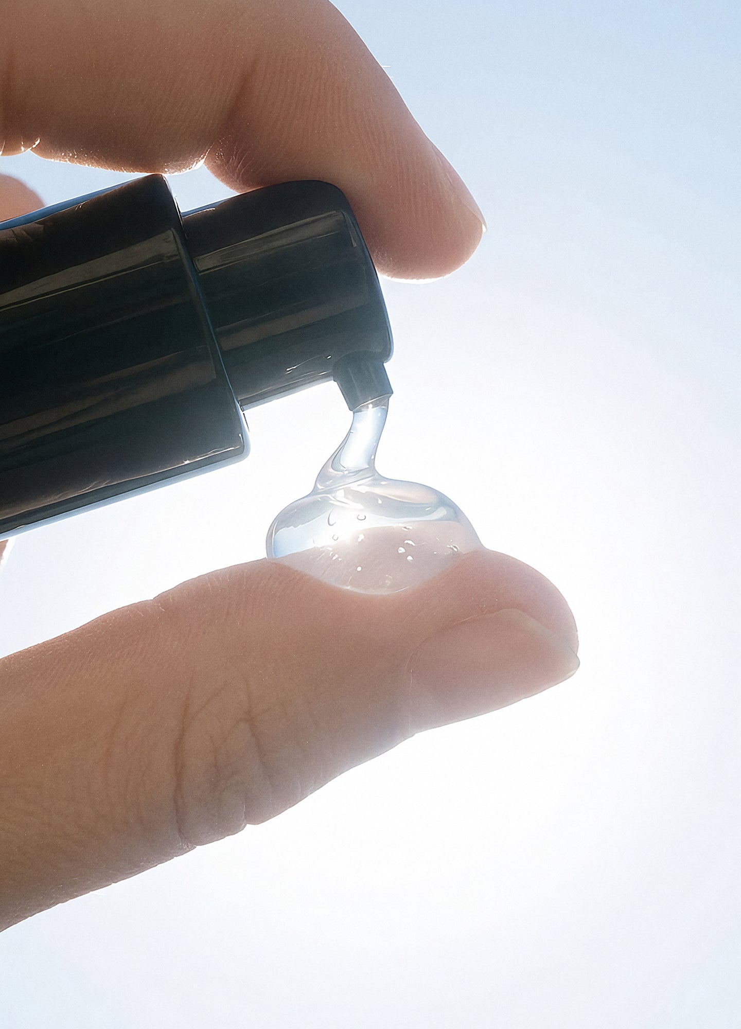 Clear gel dispensed from sleek black pump bottle onto fingertip against bright background.