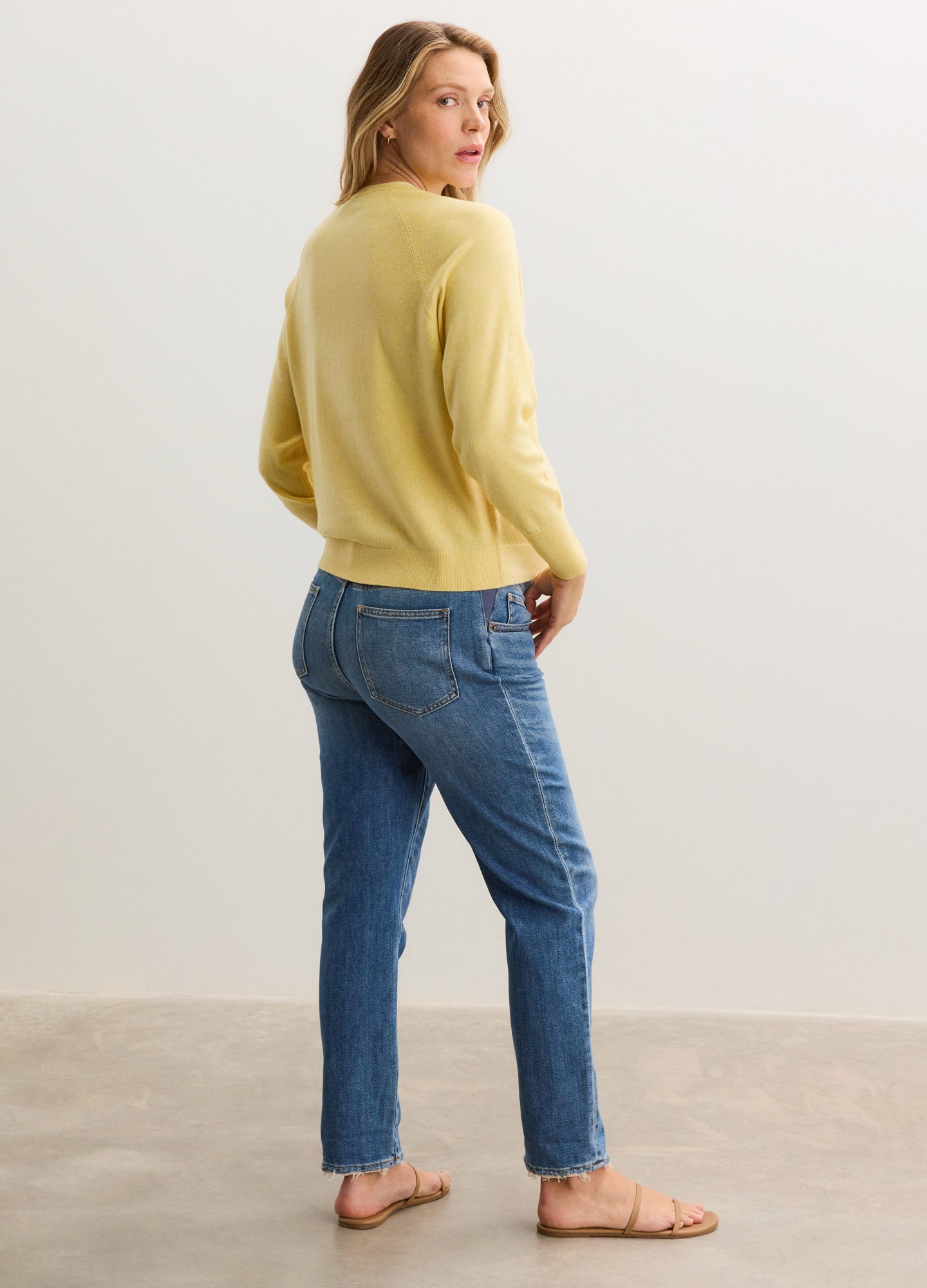 Soft yellow maternity cardigan with long sleeves paired with blue jeans and sandals on a standing pregnant model.