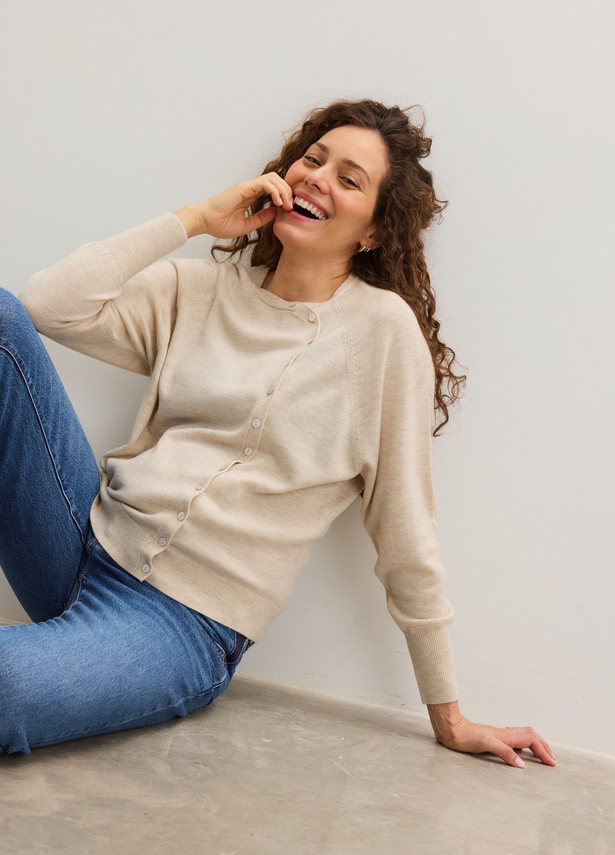 Beige soft knit maternity cardigan with front pockets and long sleeves, styled casually on a pregnant model.