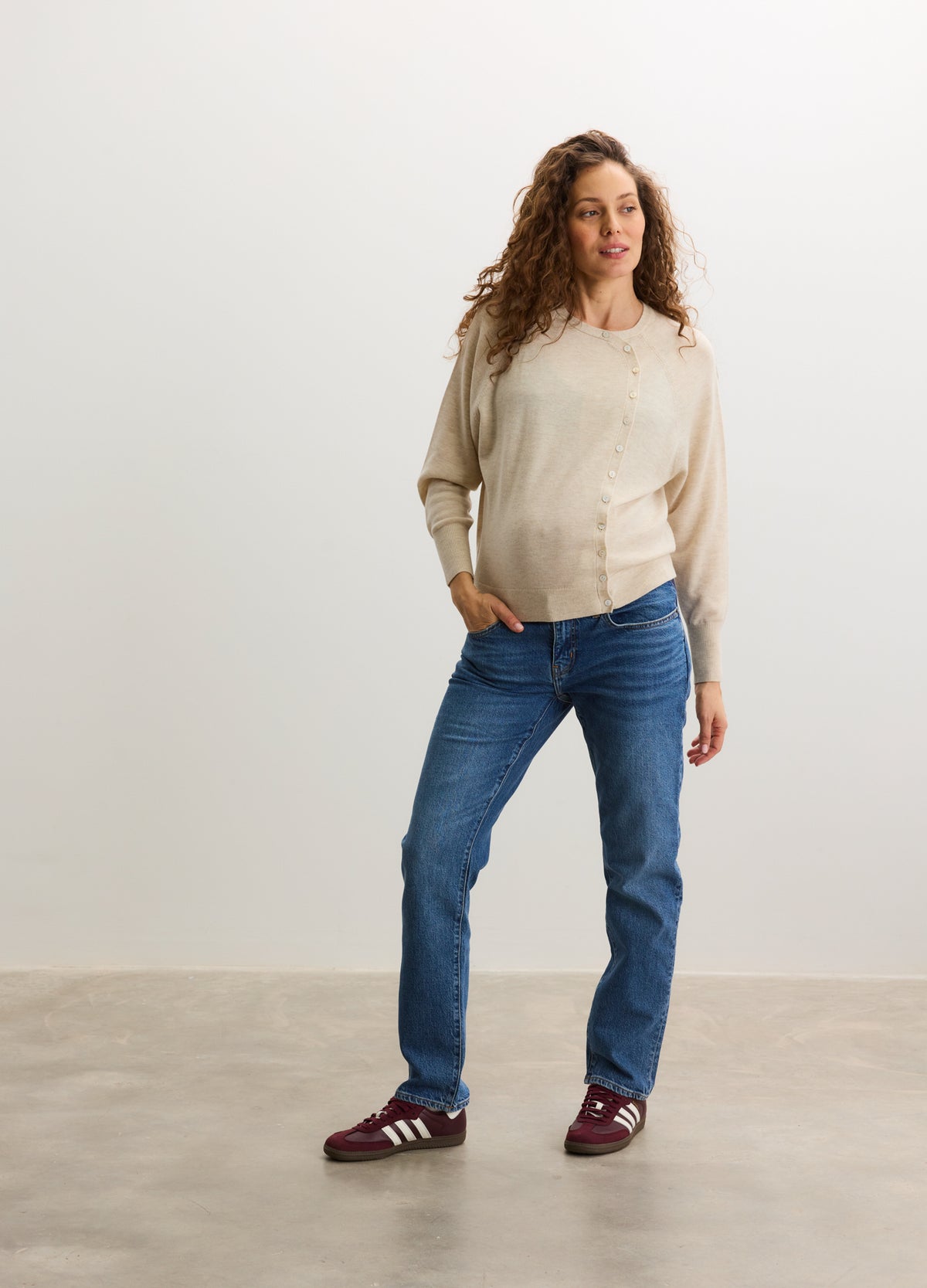 Beige maternity cardigan with button front, long sleeves, and relaxed fit paired with blue jeans and red sneakers.