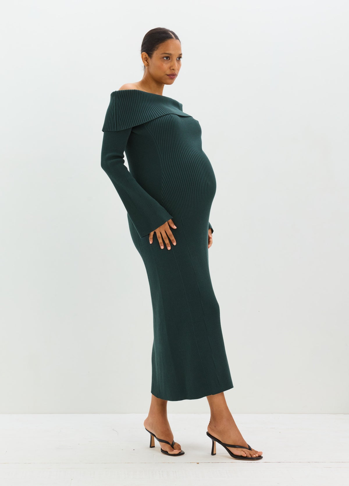 Pregnant model wearing a dark green off-the-shoulder ribbed maternity sweater dress with a fitted ankle-length silhouette.